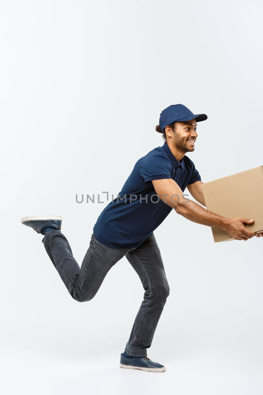 Delivery Concept - Handsome African American delivery man rush running for delivering a package for customer. Isolated on Grey studio Background. Copy Space