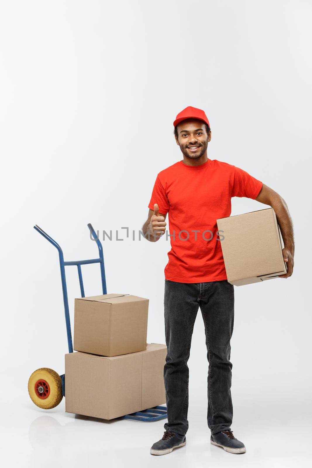 Delivery Concept - Portrait of Handsome African American delivery man or courier with hand truck and holding box. Isolated on Grey studio Background. Copy Space