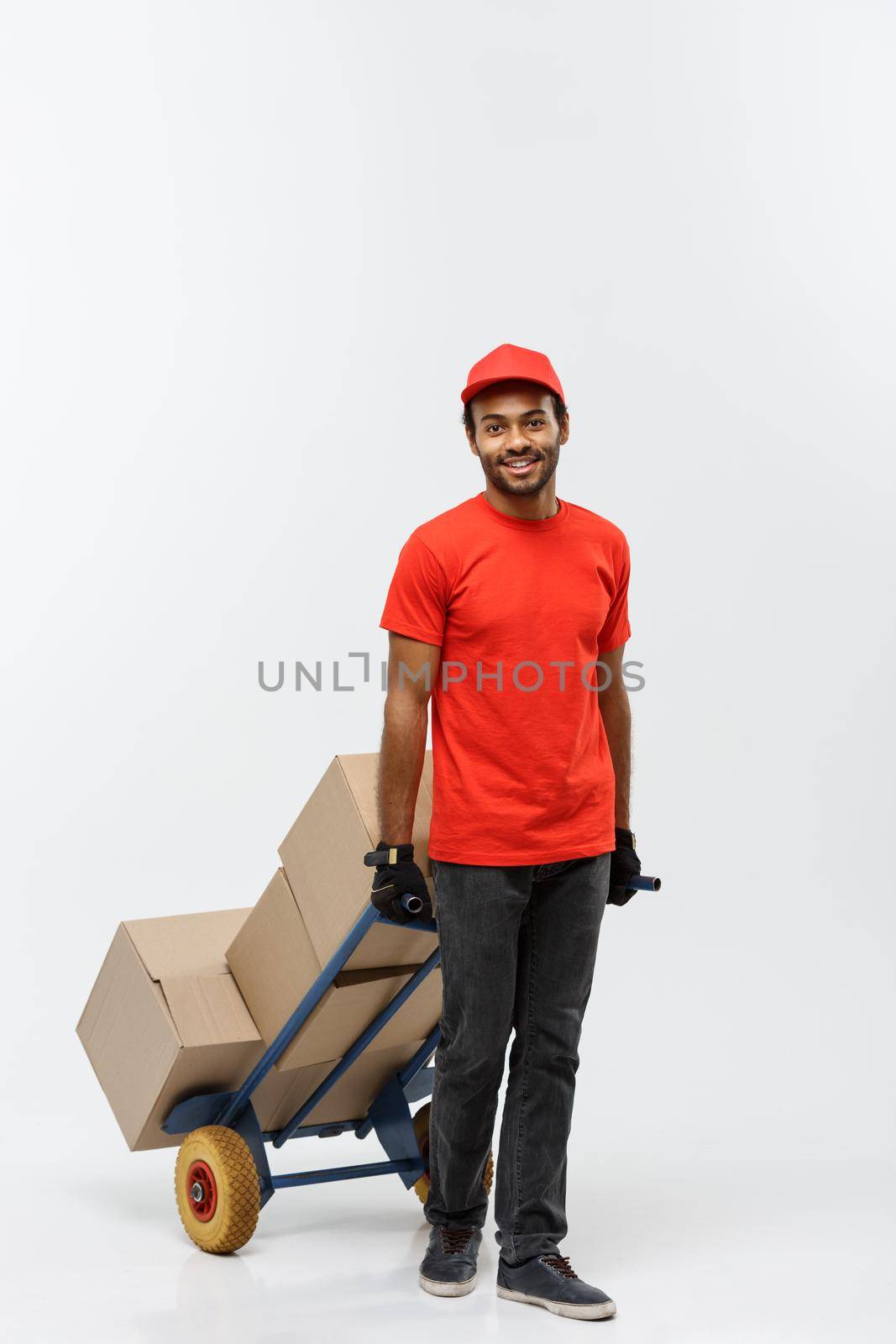 Delivery Concept - Portrait of Handsome African American delivery man or courier pushing hand truck with stack of boxes. Isolated on Grey studio Background. Copy Space