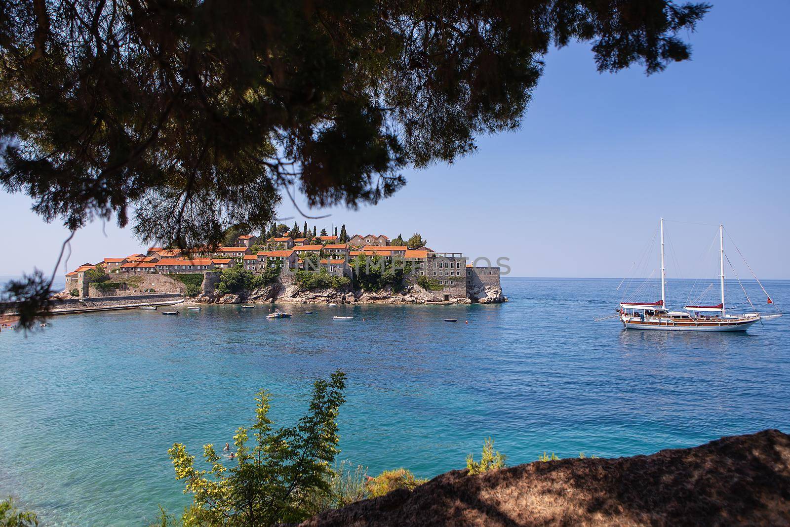 Famous architectural monument of the island resort of St. Stephen St. Stephen in the Adriatic Sea, Montenegro. The concept of vacation at sea, boat in the sea. Photo through the trees