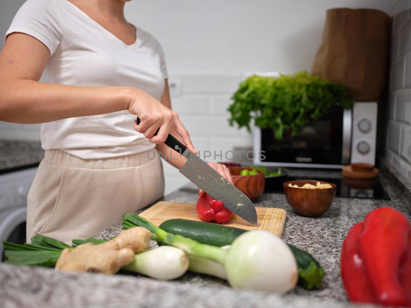 side view of a woman splitting a red pepper with a kitchen knife, vegetables around the worktop