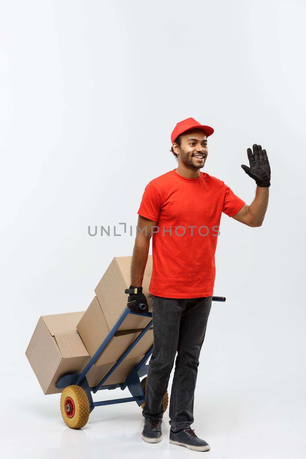 Delivery Concept - Portrait of Handsome African American delivery man or courier pushing hand truck with stack of boxes. Isolated on Grey studio Background. Copy Space. by Benzoix