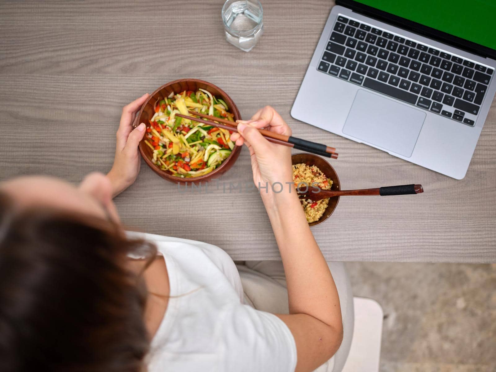 top view of a woman eating with chopsticks in front of the computer, over a wooden table