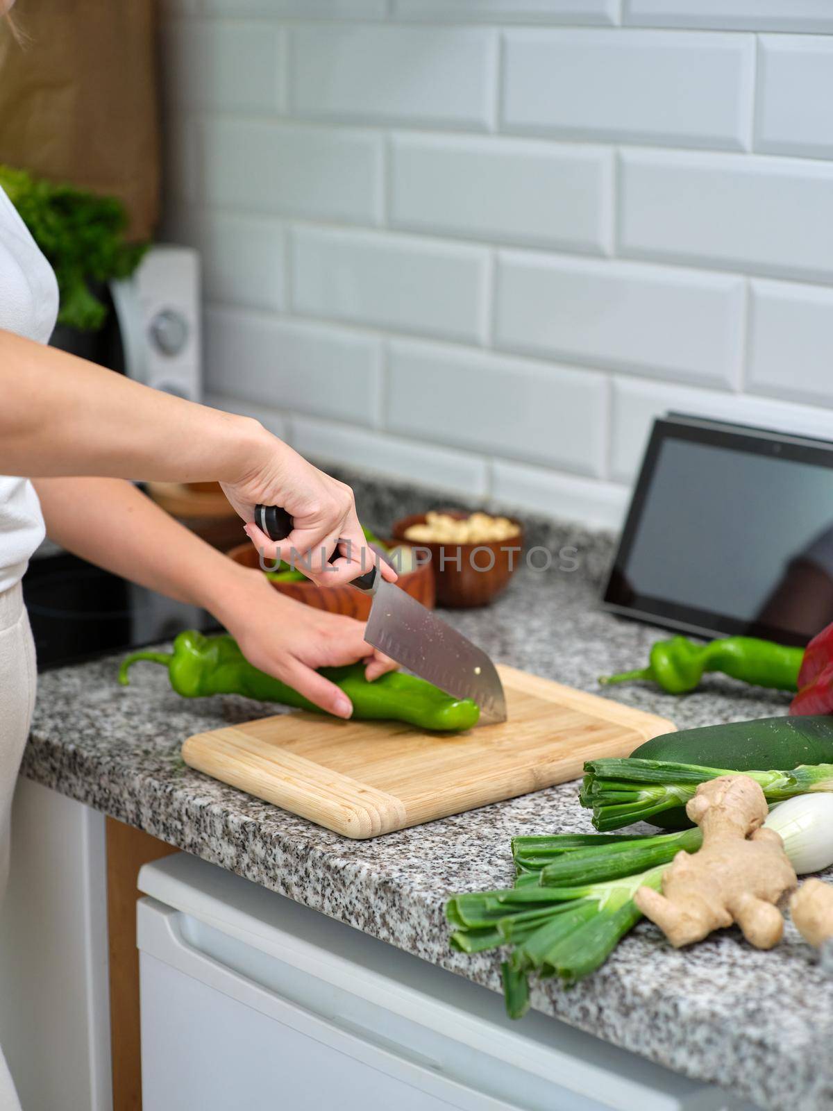 cook chopping vegetables on a wooden plank, tablet leaning against the wall to see the recipe by WesternExoticStockers