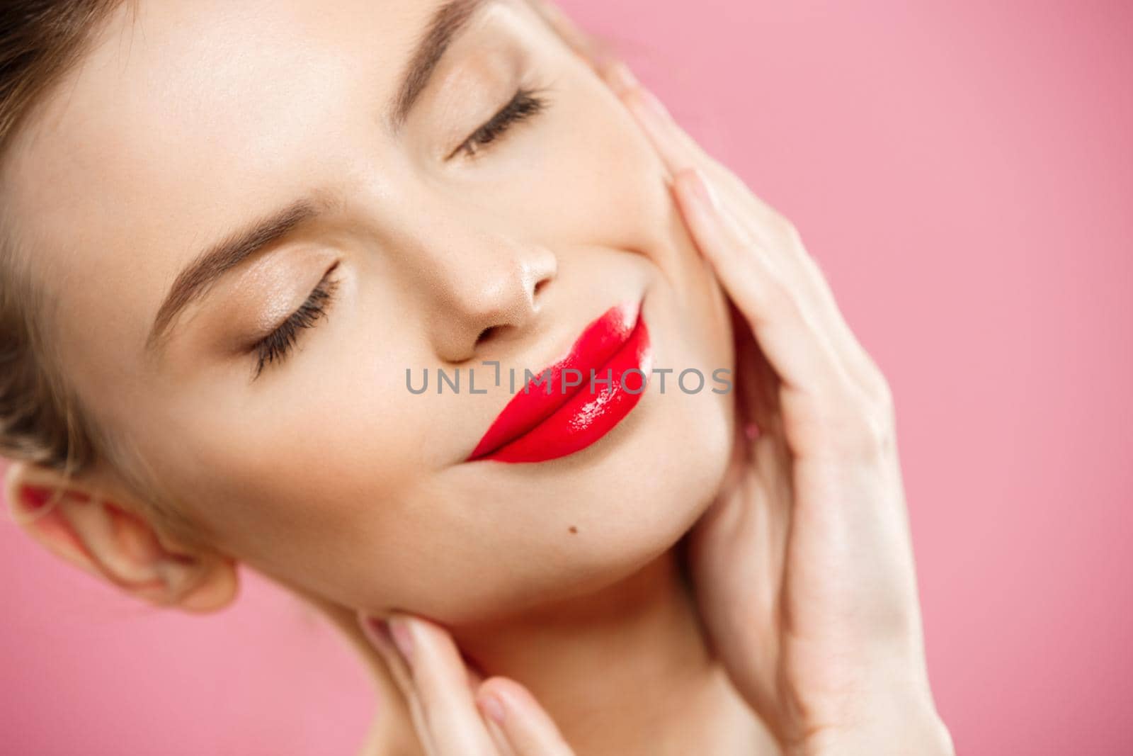 Beauty concept - Gorgeous Young Brunette Woman face portrait. Beauty Model Girl with bright eyebrows, perfect make-up, red lips, touching her face. Isolated on pink background