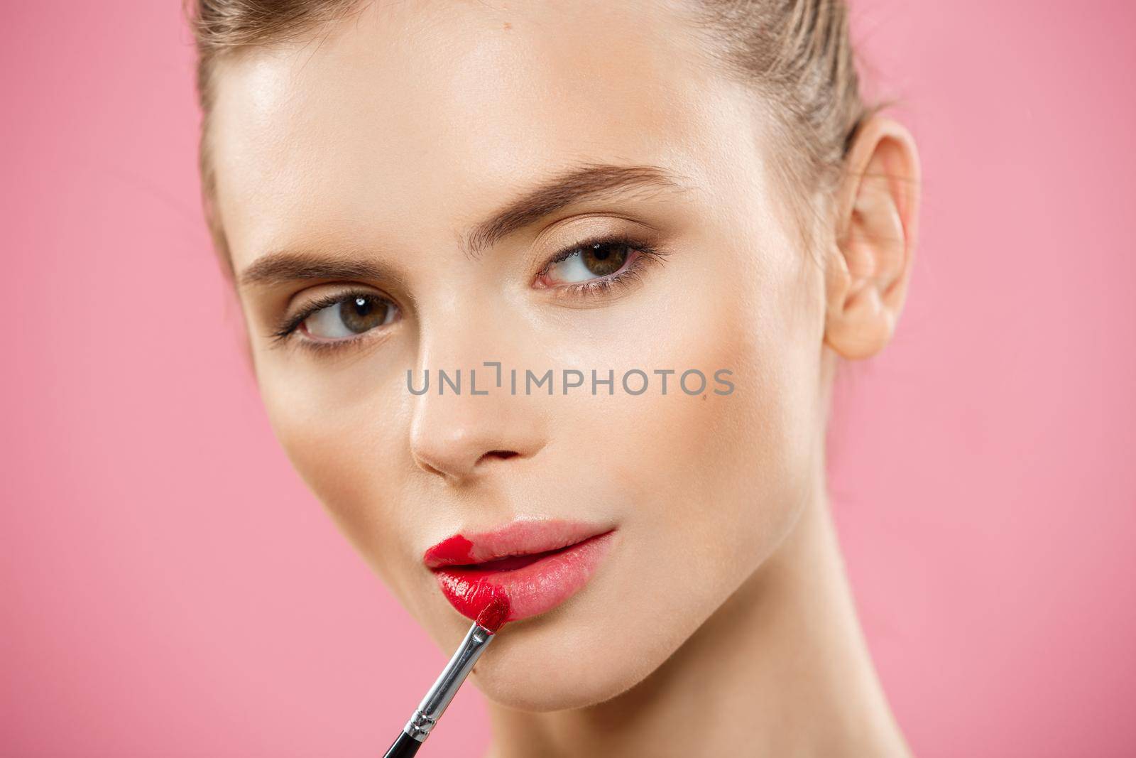 Beauty Concept - Woman applying red lipstick with pink studio background. Beautiful girl makes makeup