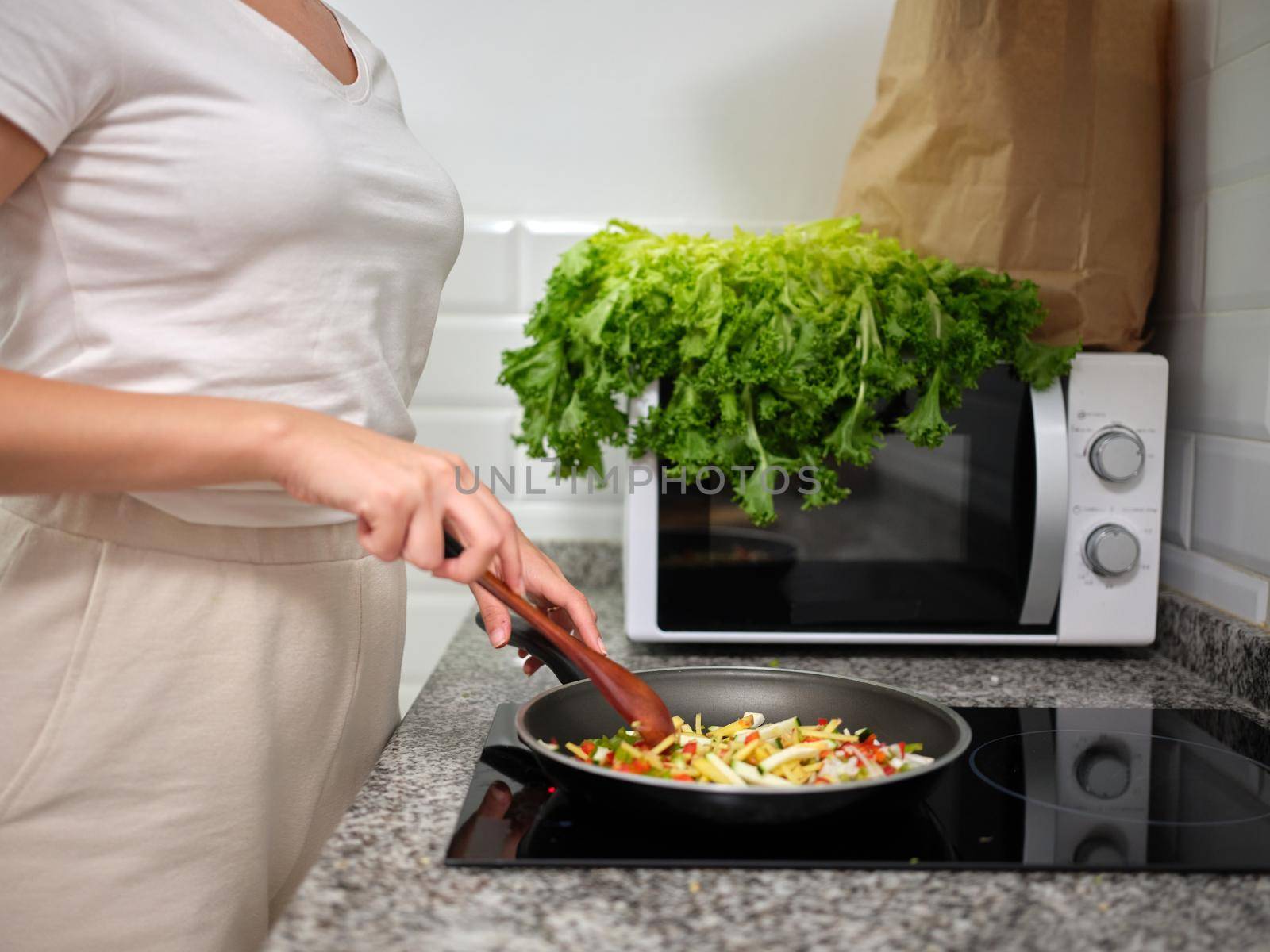 woman stirring the vegetables in the frying pan with a wooden paddle, horizontal side view cut out