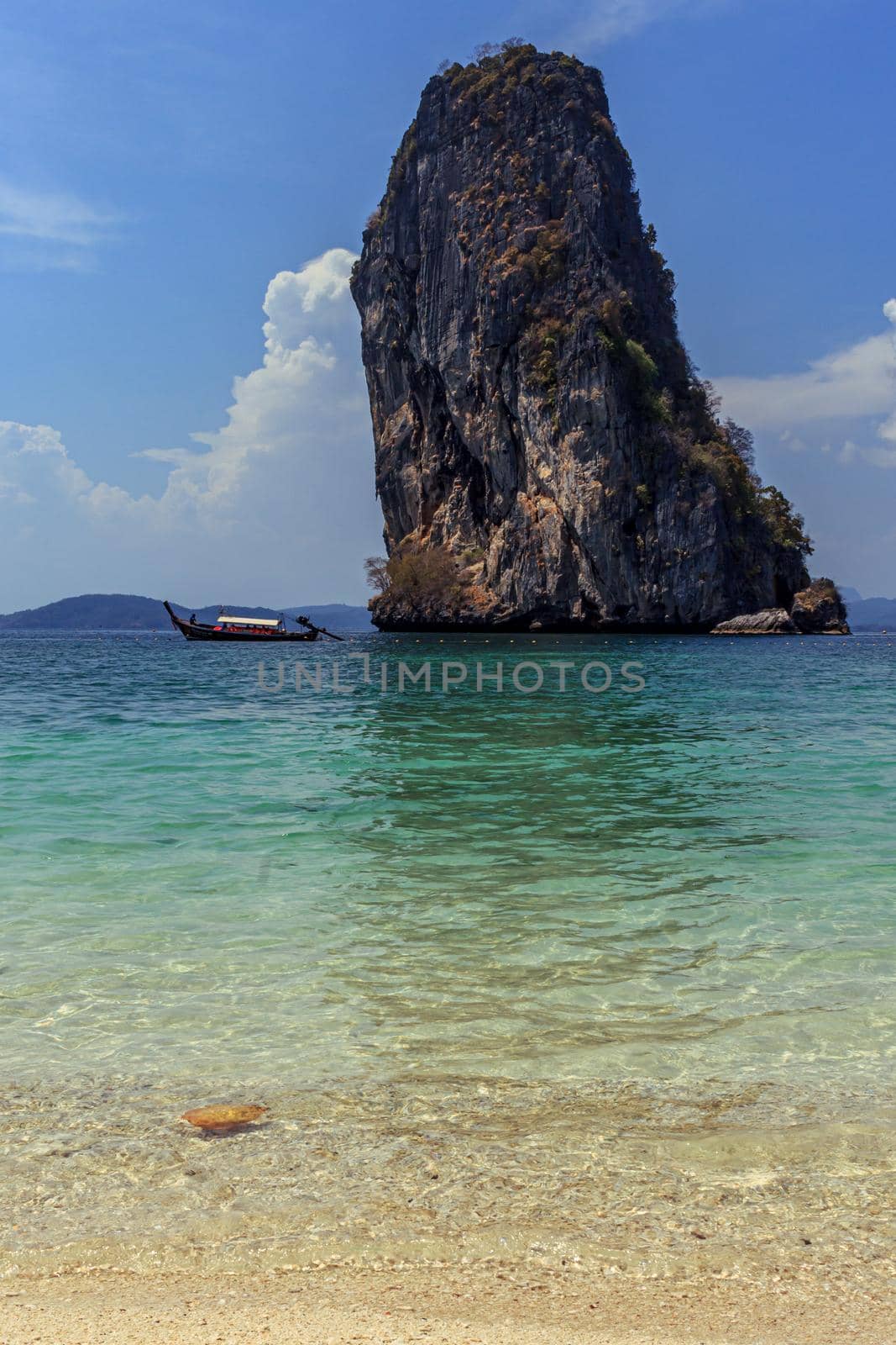 Thailand traditional wood long tail boat in turquoise blue water, islands tour, huge rock background