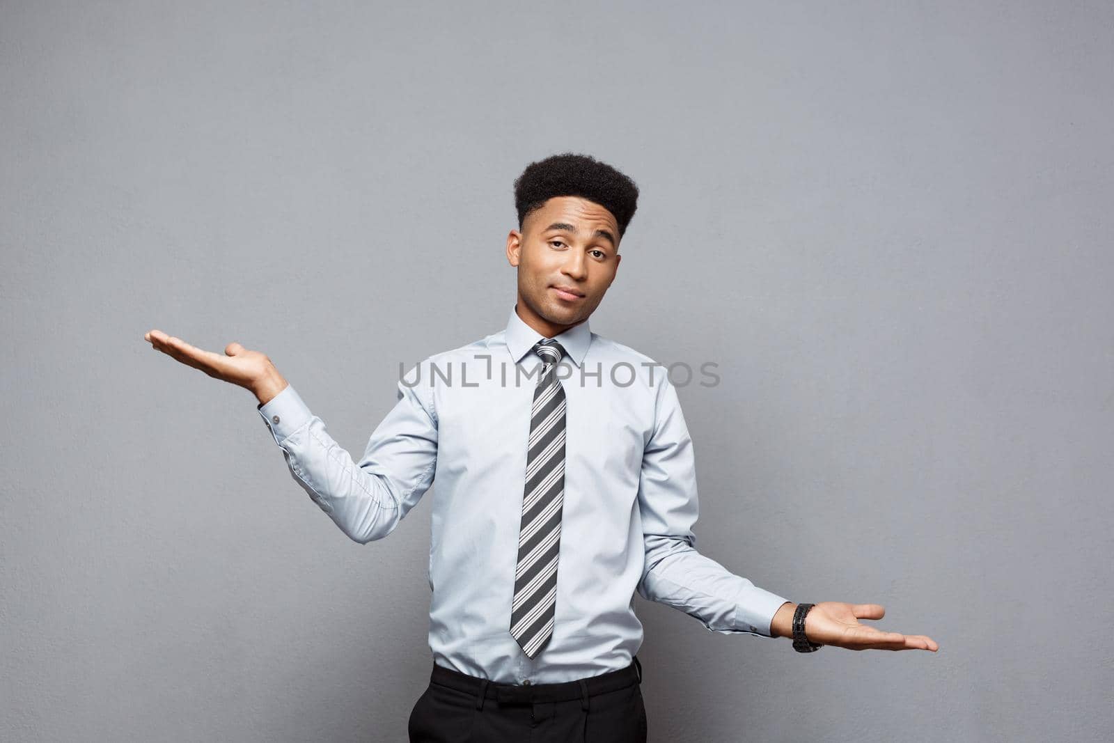Business Concept - Confident thoughtful young African American showing balancing hands on side over grey background. by Benzoix