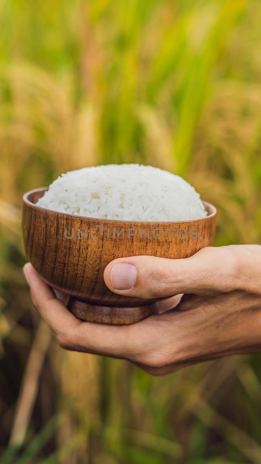 The hand holds a cup of boiled rice in a wooden cup, against the background of a ripe rice field. VERTICAL FORMAT for Instagram mobile story or stories size. Mobile wallpaper