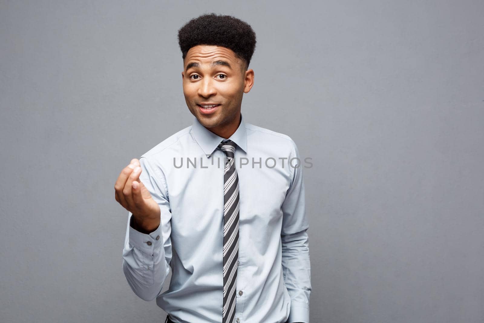 Business Concept - Confident cheerful young African American showing hands in front of him with surprising expression over grey background
