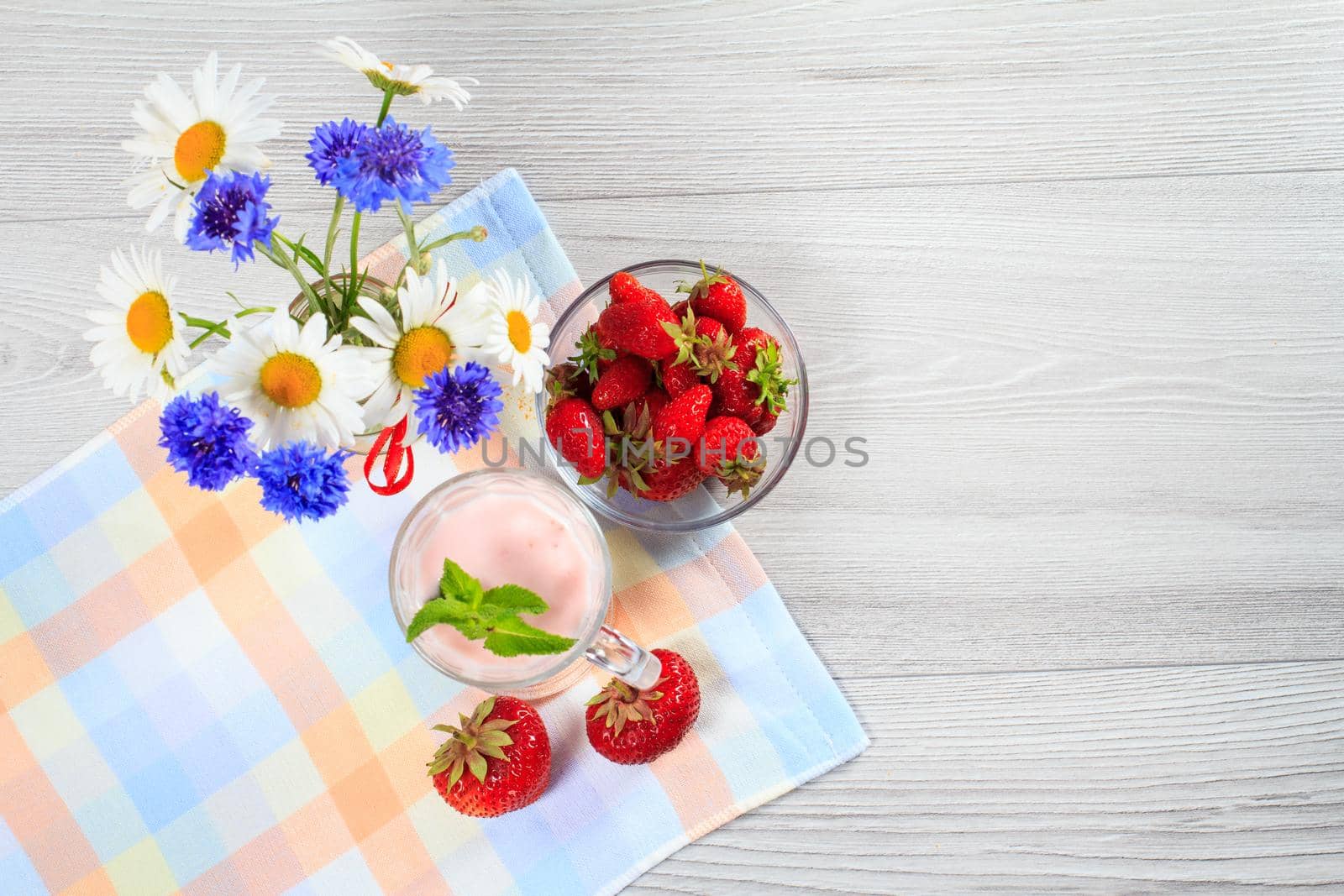 Strawberry yogurt in a glass with fresh strawberries, chamomile, cornflowers on a wooden table with a napkin Top view