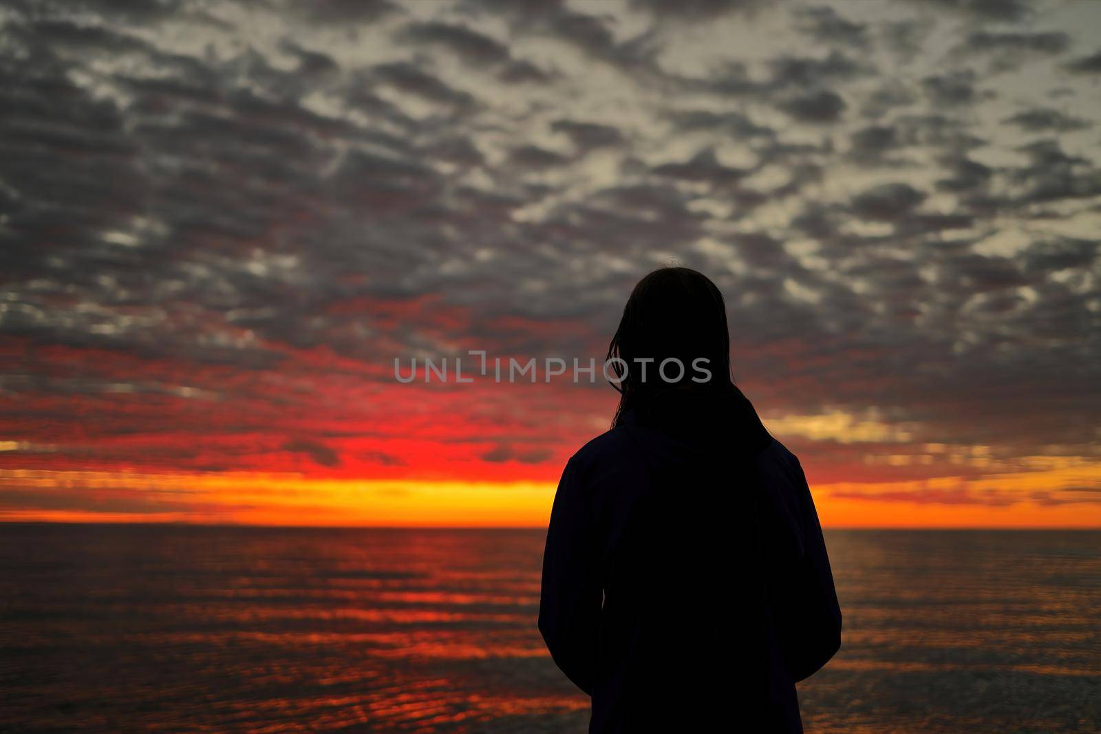 Silhouette of Young Adolescent Girl Looks in Awe, Wonder, and Admiration at a Magnificent Sunset Sky while Standing on Wasaga Beach with Georgian Bay in background. Rear View. High quality photo