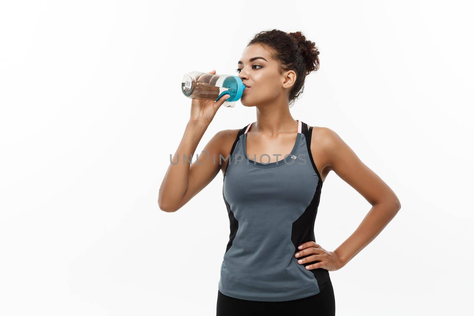 Healthy and Fitness concept - beautiful African American girl in sport clothes drinking water after workout. Isolated on white studio background by Benzoix