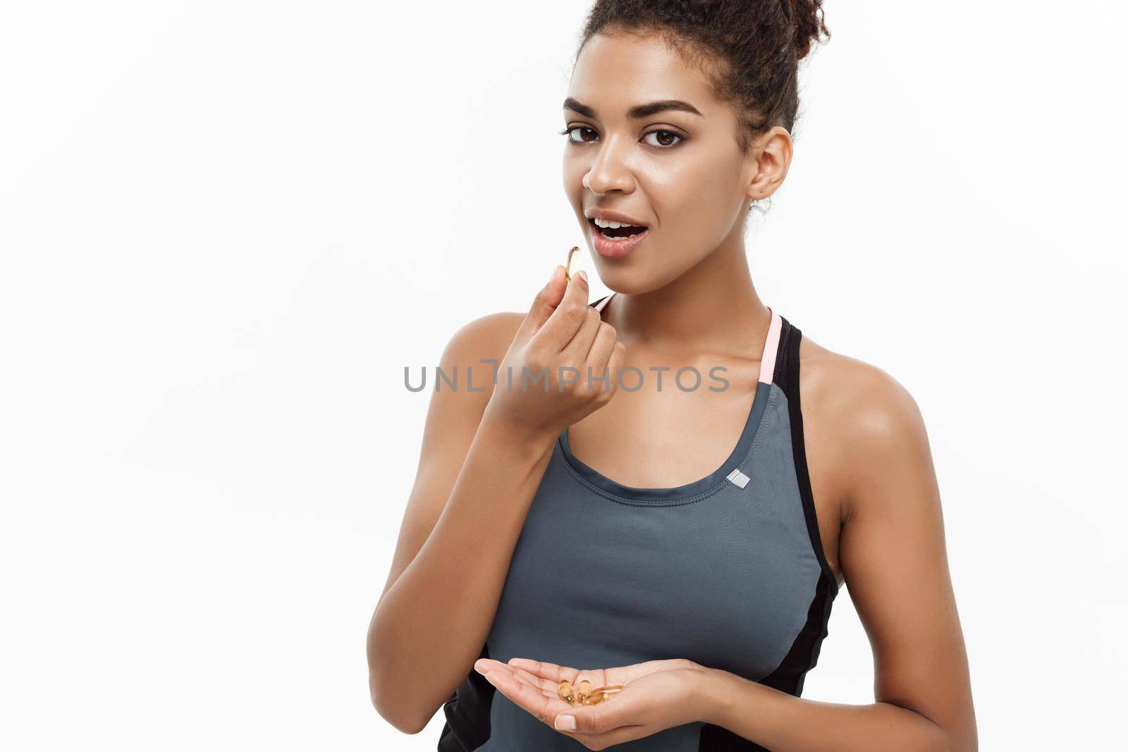 healthcare concept - Closeup portrait of beautiful African American taking a pill of Cod liver oil. Isolated on white studio background.