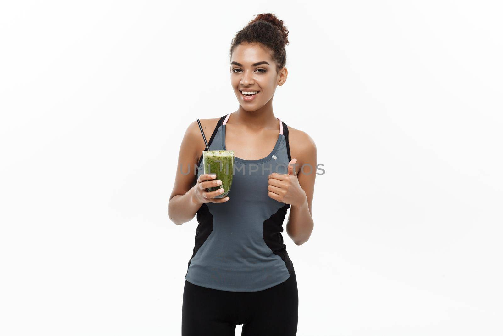 Healthy and Fitness concept - Beautiful American African lady in fitness clothing drinking healthy vegetable drink. Isolated on white background. by Benzoix