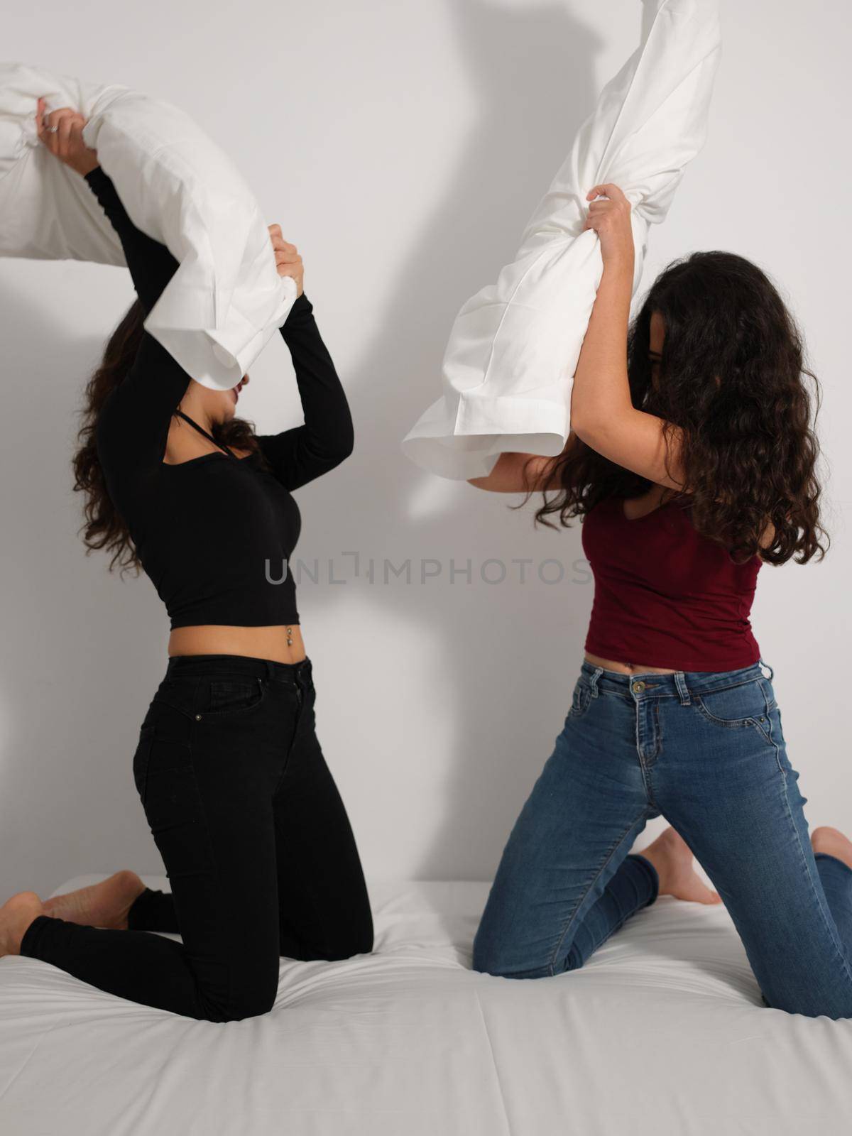 Vertical image of two latin girls playing pillow fight in bed.