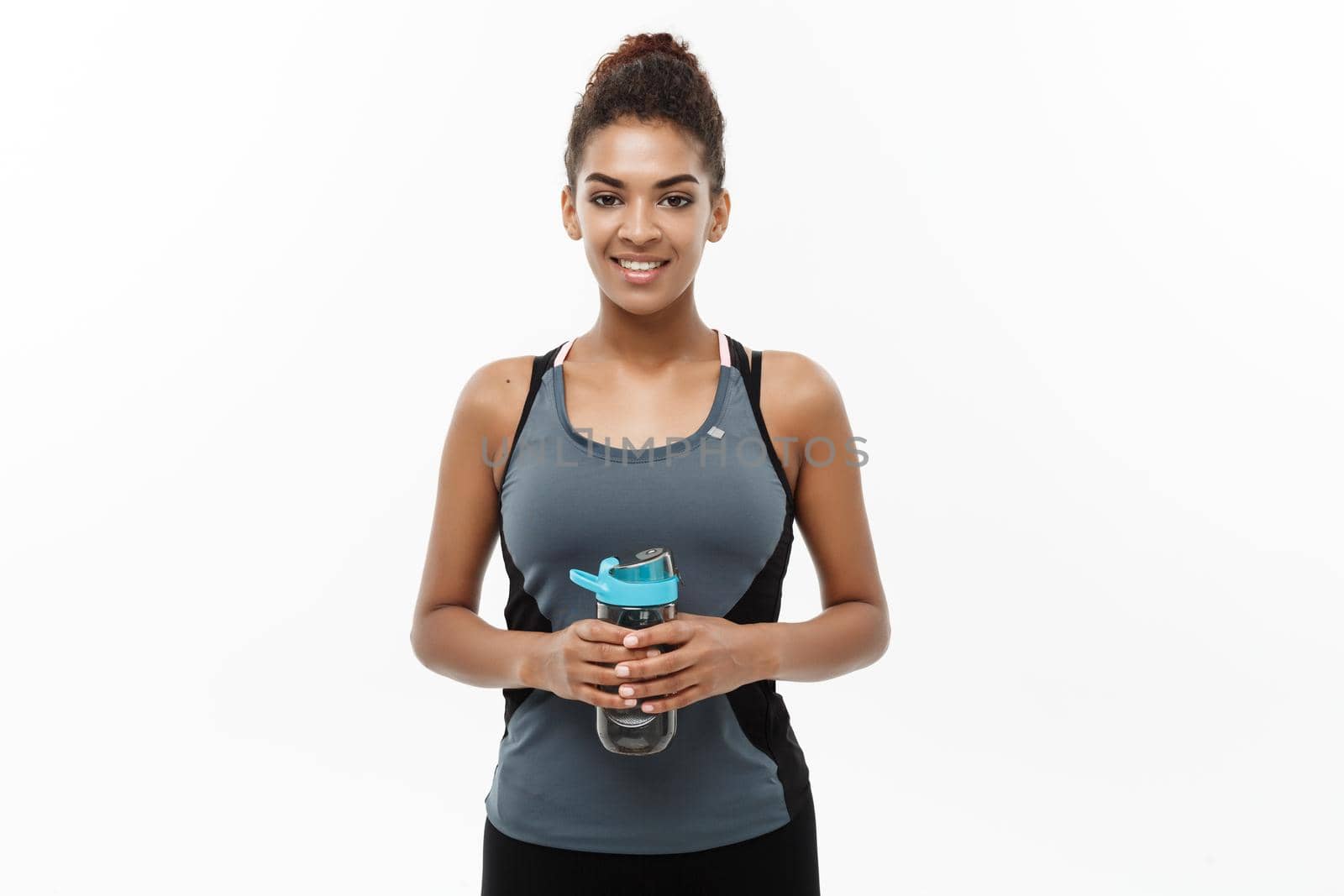 Healthy and Fitness concept - beautiful African American girl in sport clothes holding water bottle after workout. Isolated on white studio background by Benzoix