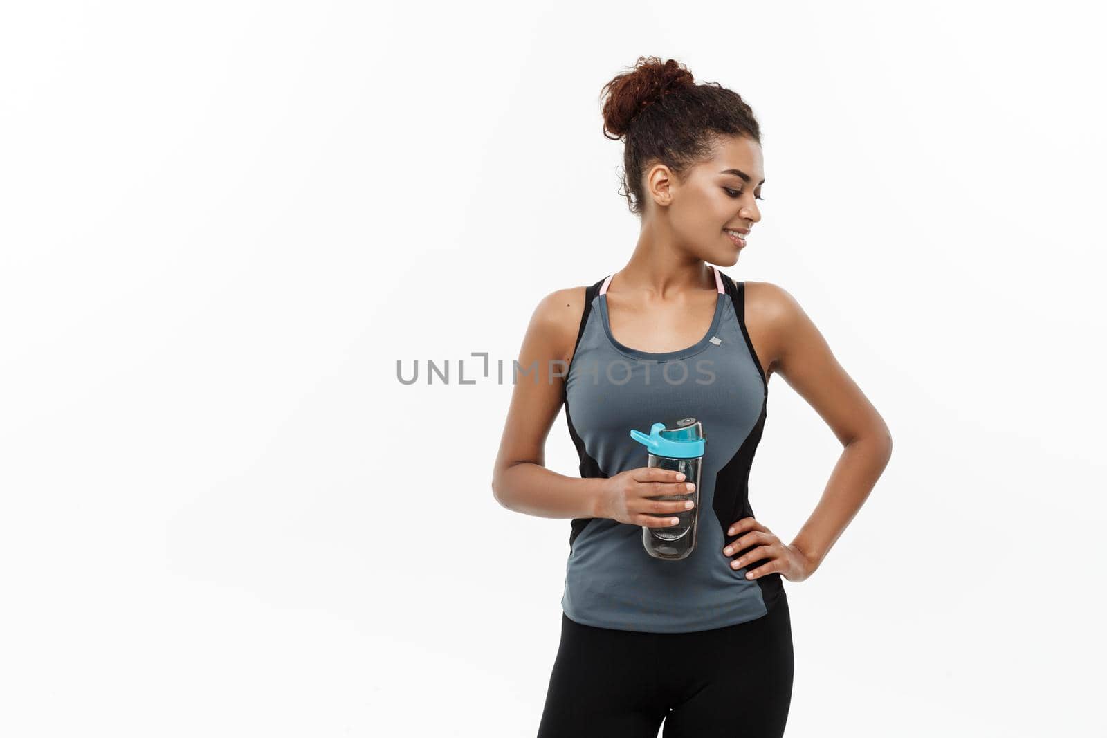 Healthy and Fitness concept - beautiful African American girl in sport clothes holding water bottle after workout. Isolated on white studio background.