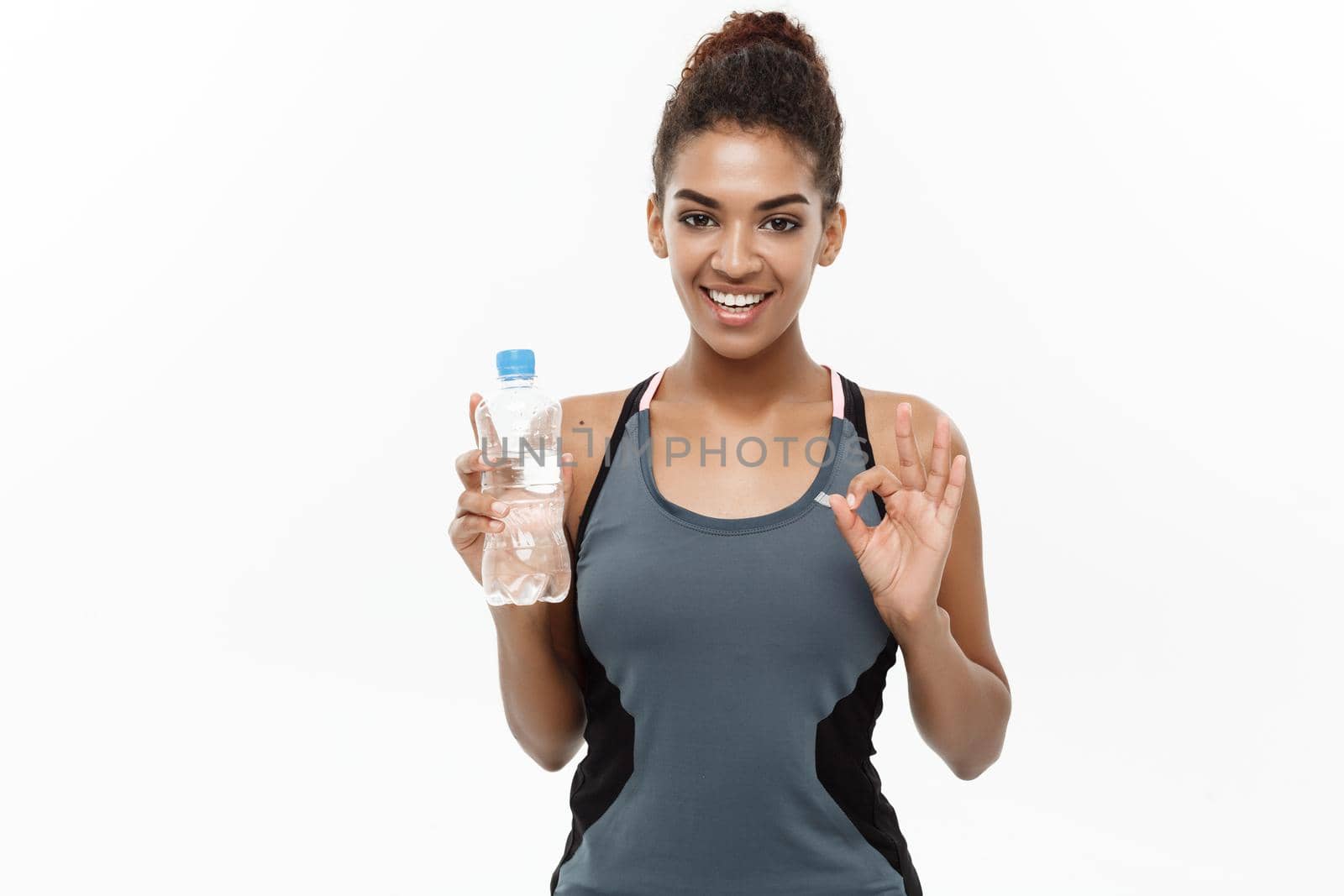 Healthy and Fitness concept - beautiful African American girl in sport clothes holding plastic water bottle after workout. Isolated on white studio background by Benzoix