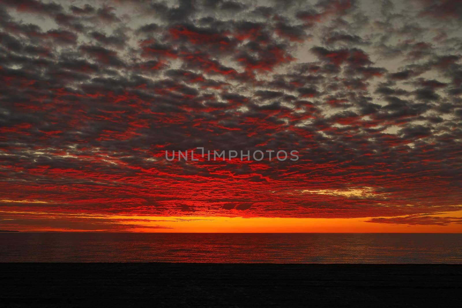 Beautiful, dramatic, fiery sunset, sunrise sky in orange, red, yellow, pink and blue colors. Perfect for sky replacement or for representing feelings or emotions. With water lake or ocean in background.