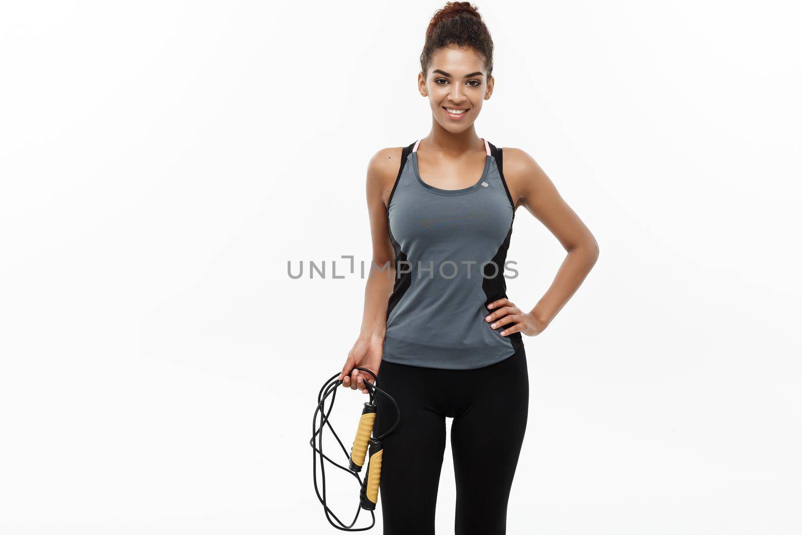 Sport, training, lifestyle and Fitness concept - portrait of beautiful happy African American woman exercising with jumping rope. Isolated on white studio background