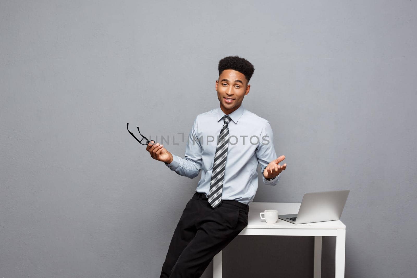 Business Concept - portrait of african american businessman with glasses having coffee sitting at a desk using a laptop. by Benzoix