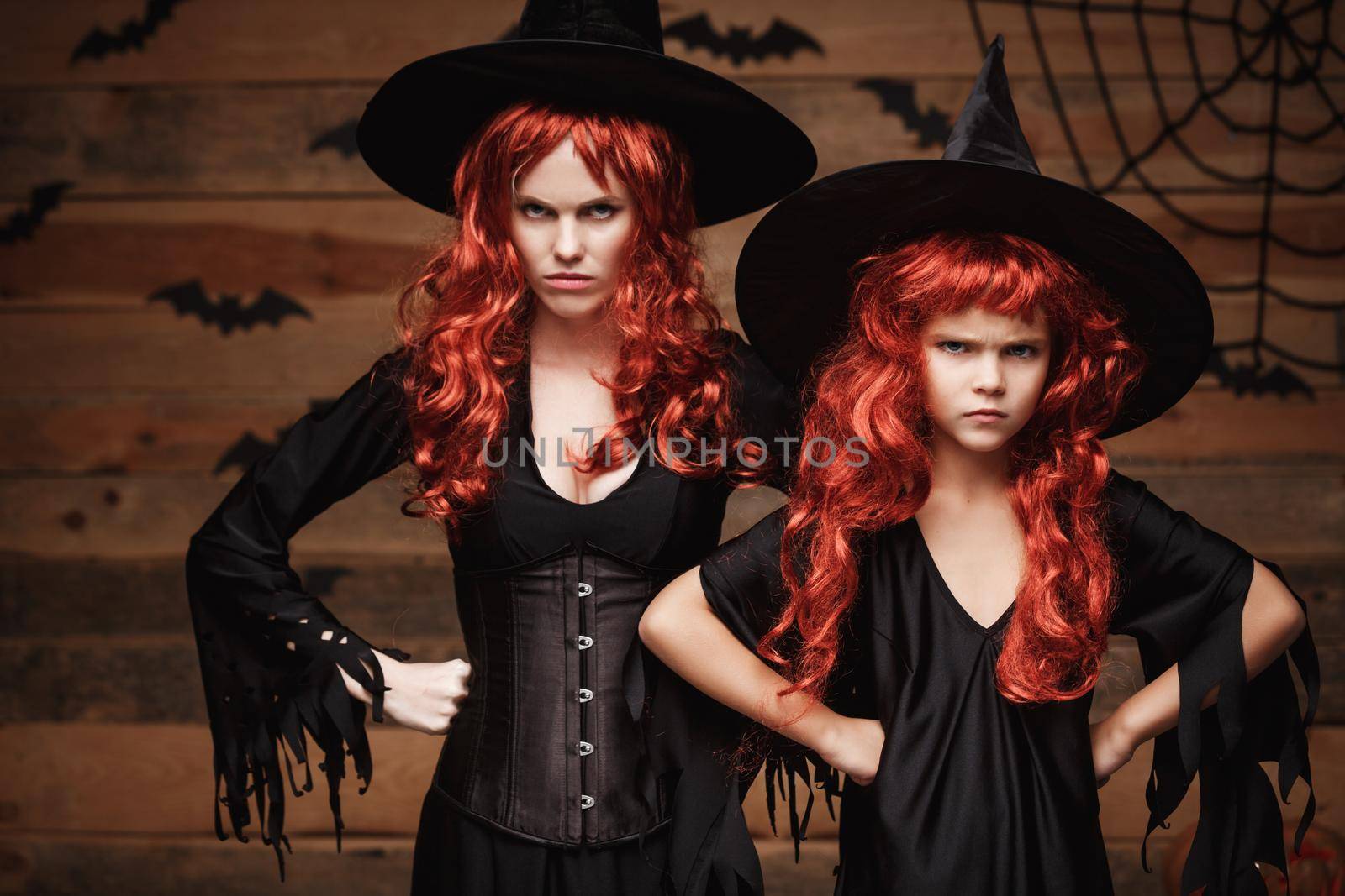Halloween Concept - Beautiful caucasian mother and her daughter with long red hair in witch costumes with angry fussy facial expression