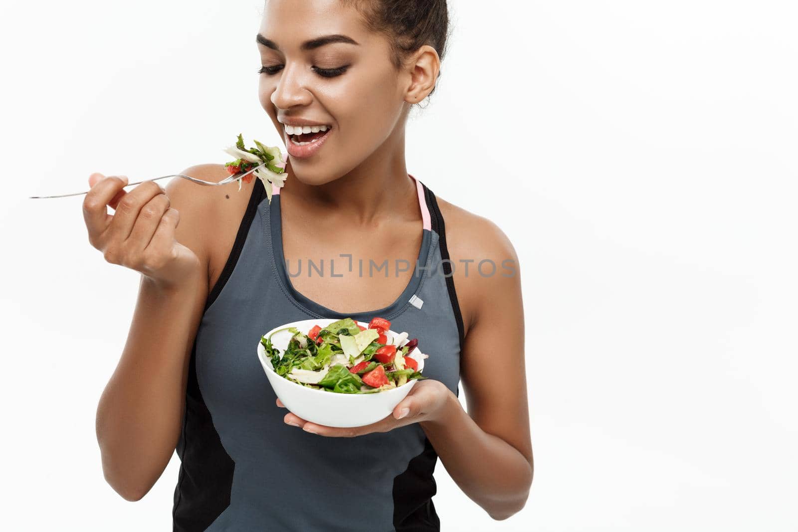 Healthy and Fitness concept - Beautiful American African lady in fitness clothes on diet eating fresh salad. Isolated on white background