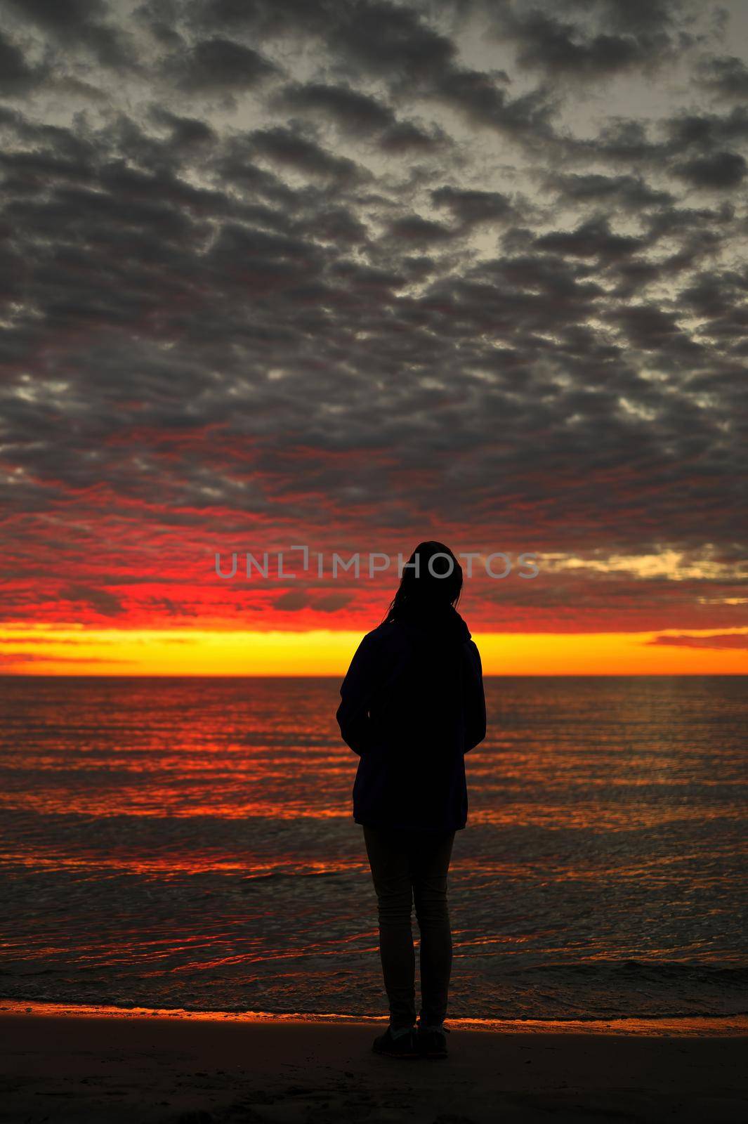 Silhouette of Young Adolescent Girl Looks up in Awe, Wonder, and Admiration at a Magnificent Sunset Sky while Standing on Wasaga Beach with Georgian Bay in background. Rear View. High quality photo