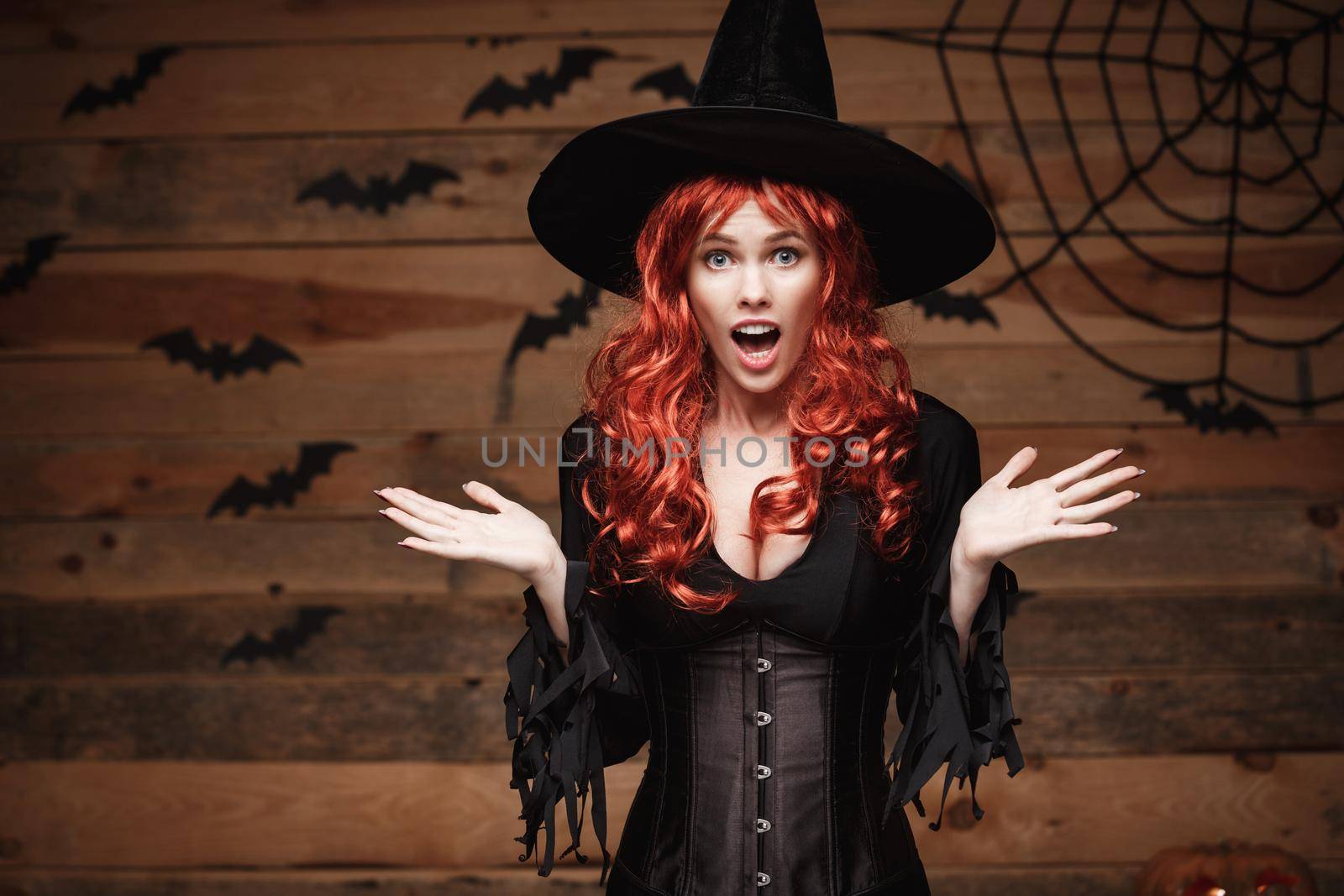 Halloween witch concept - Happy Halloween red hair Witch holding posing with shocked face over old wooden studio background