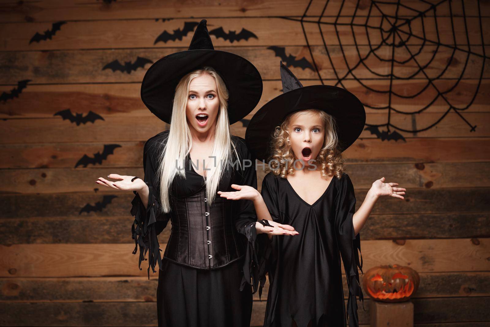 Halloween Concept - cheerful mother and her daughter in witch costumes shocking with something