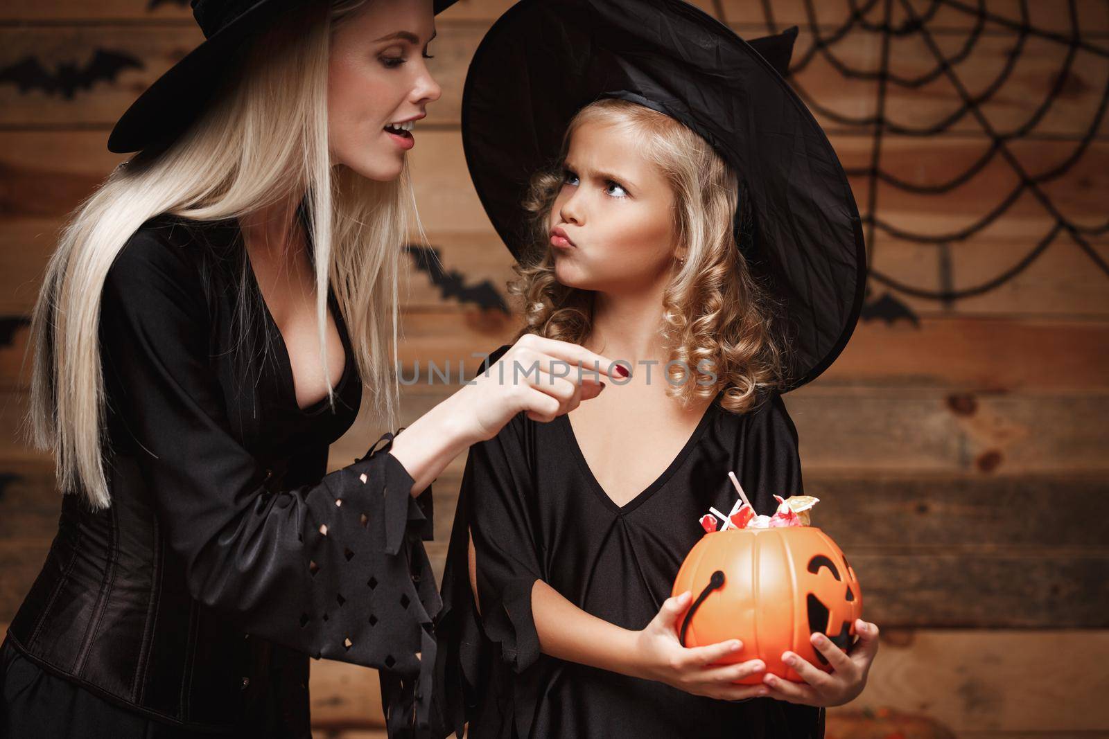 Halloween Concept - beautiful caucasian mother playing with her little daugther enjoy with Halloween candy and sweet over bats and spider web on Wooden studio background. by Benzoix