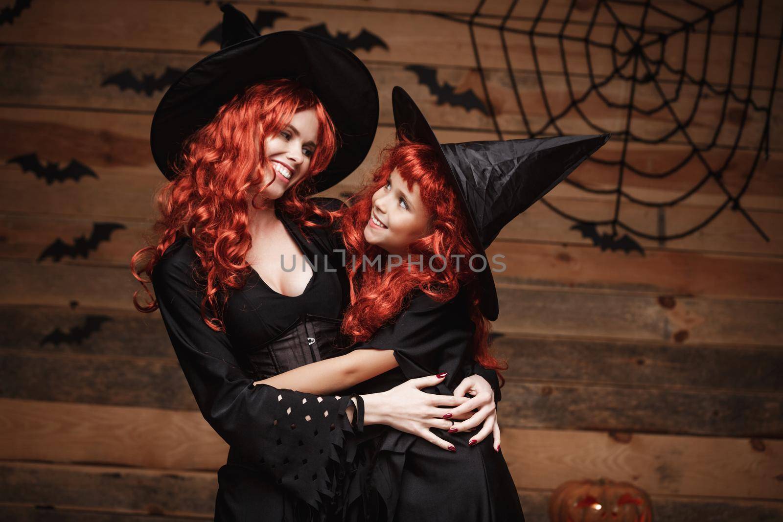 Halloween Concept - Beautiful caucasian mother and her daughter with long red hair in witch costumes happy smiling and hug each other