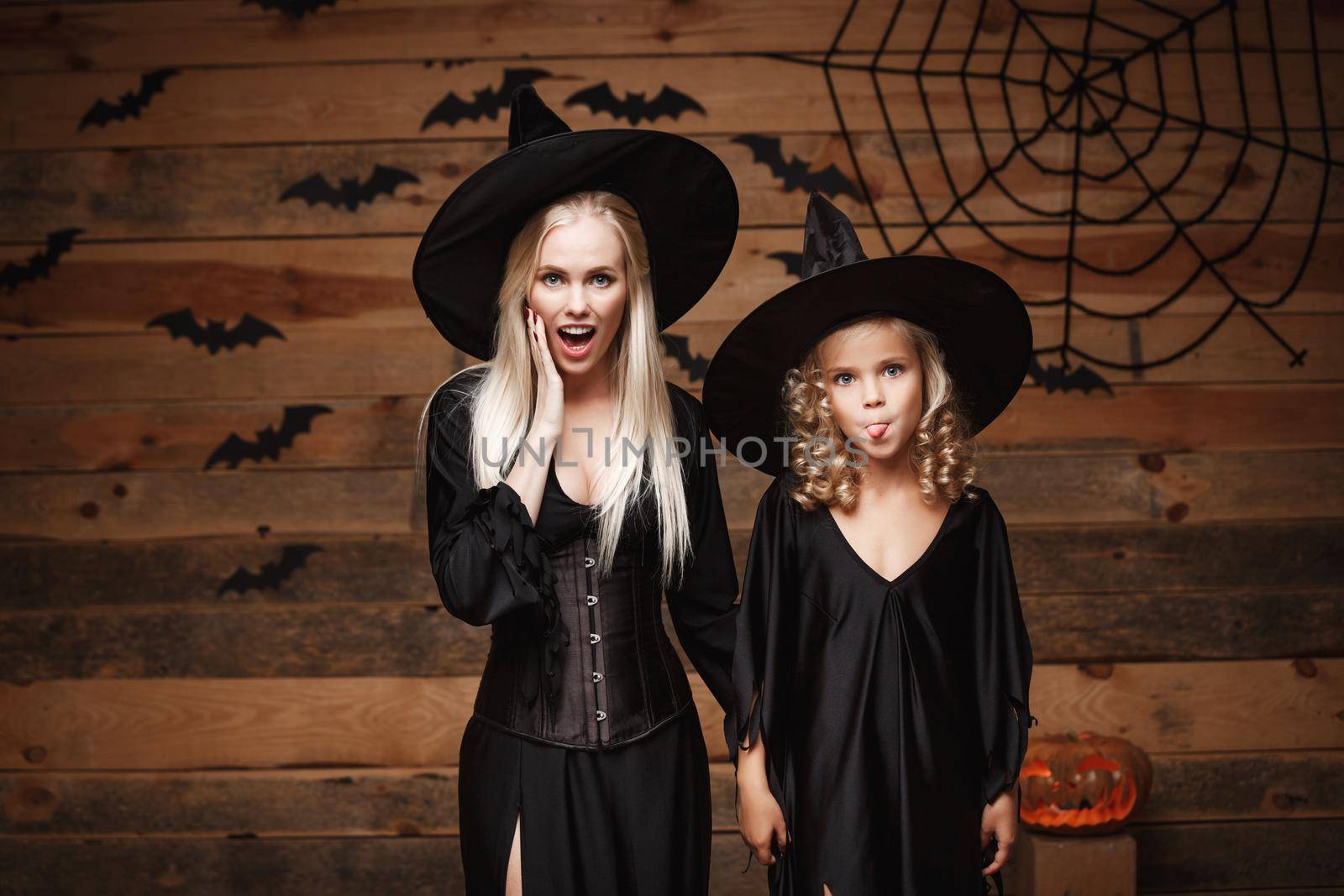 Halloween Concept - cheerful mother and her daughter in witch costumes shocking with something