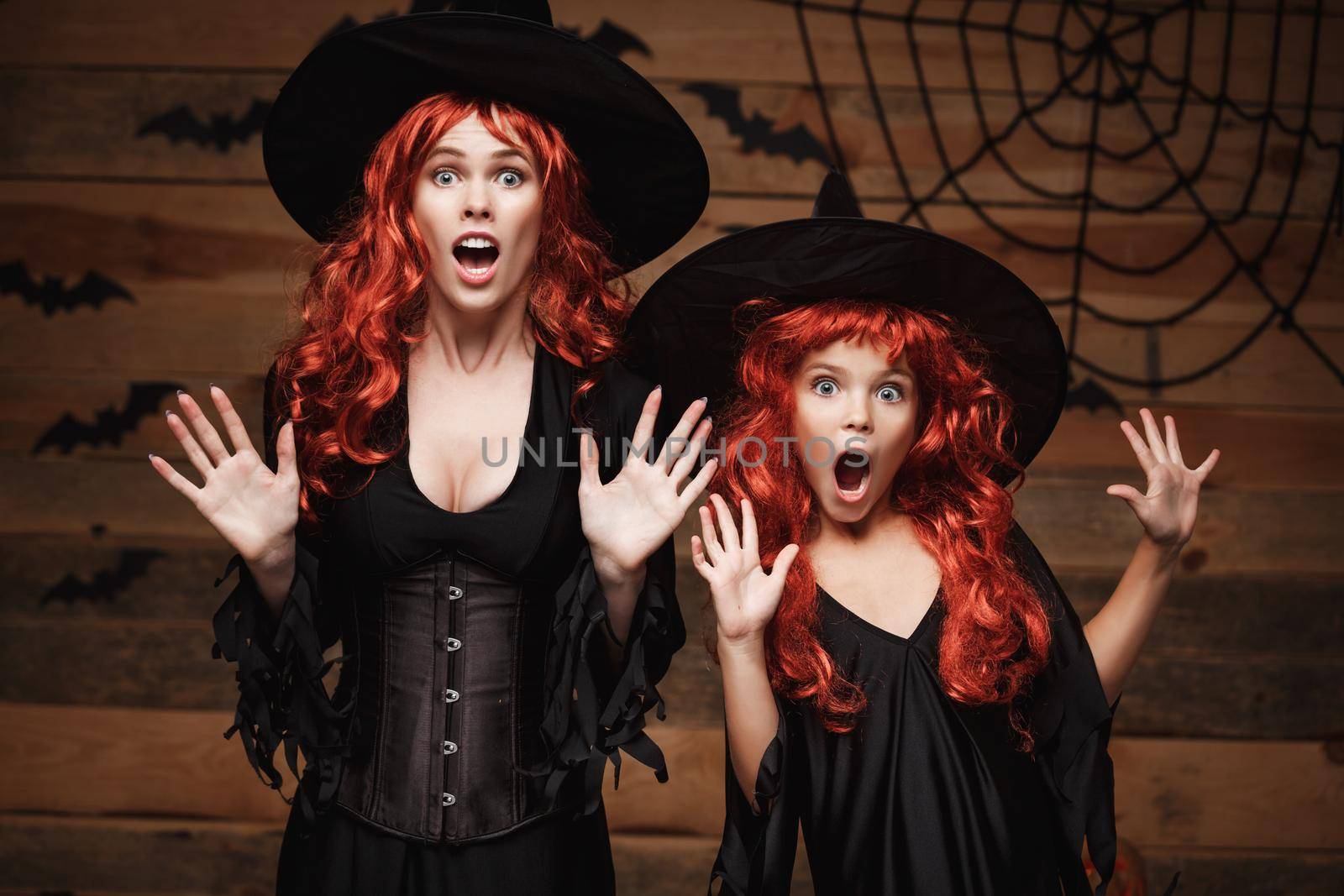 Halloween Concept - Beautiful caucasian mother and her daughter with long red hair in witch costumes with shocked facial expression. by Benzoix