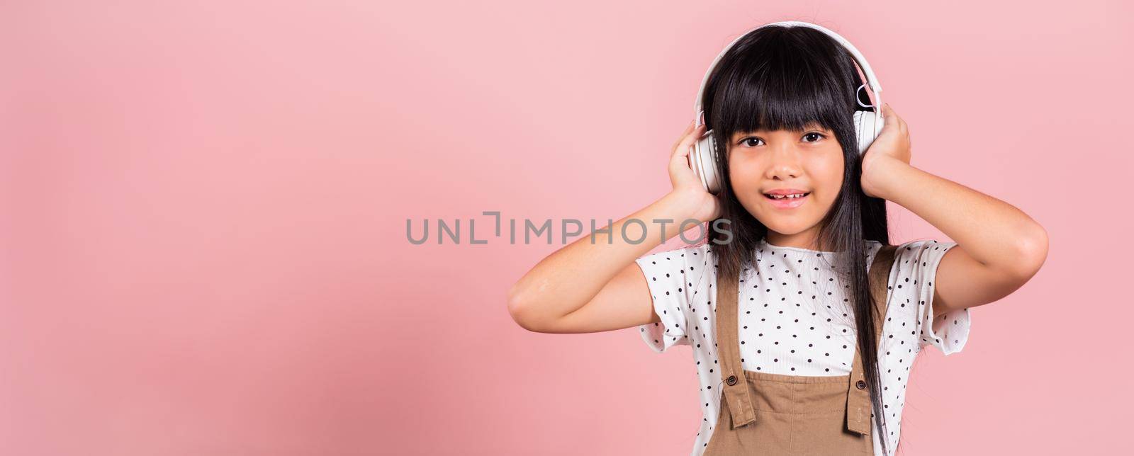 Asian little kid 10 years old smiling listening music wearing wireless headset on her head at studio shot isolated on pink background, Happy child girl lifestyle listen music with headphones