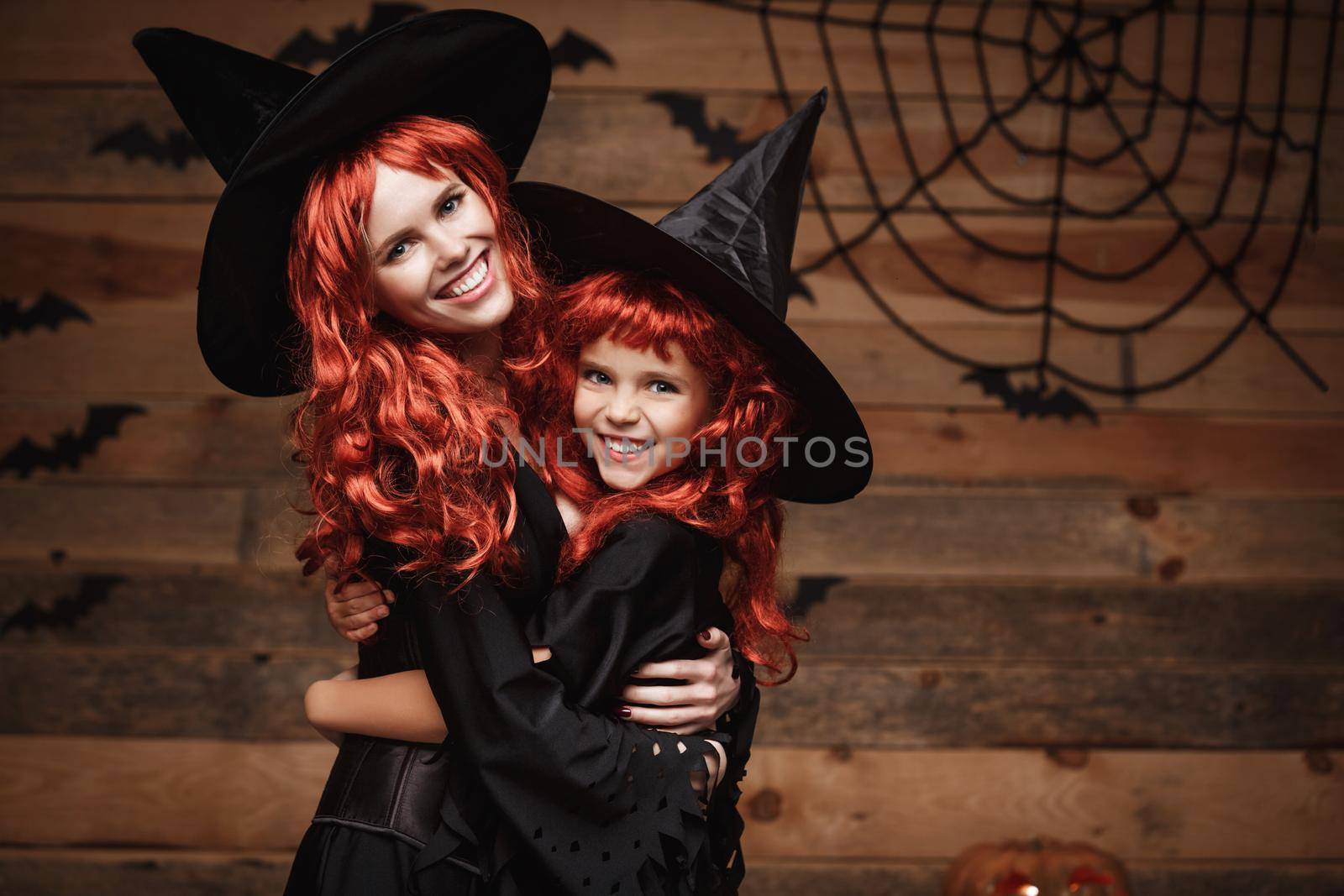Halloween Concept - Beautiful caucasian mother and her daughter with long red hair in witch costumes happy smiling and hug each other. by Benzoix