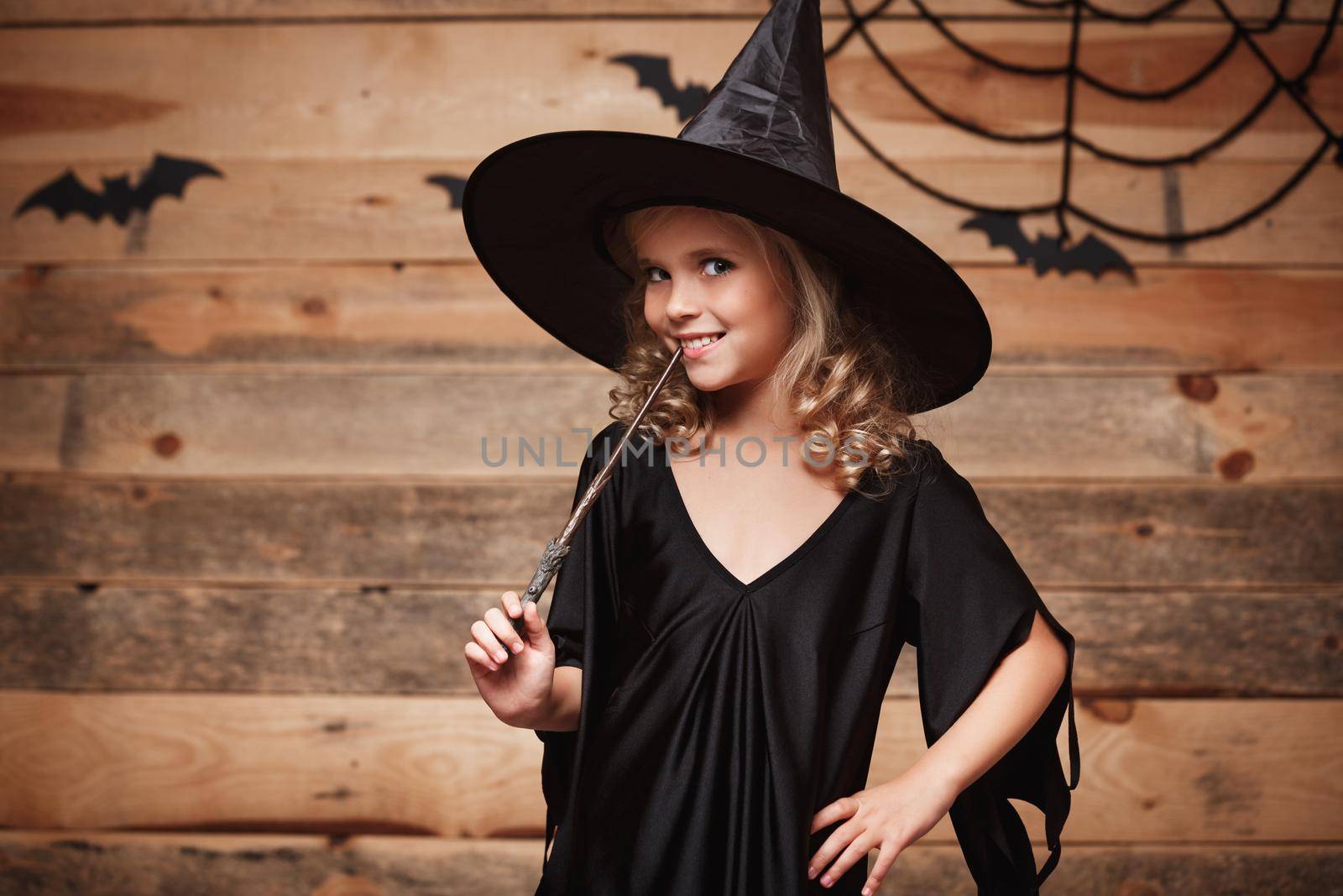 Halloween Witch concept - little witch child enjoy playing with magic wand. over bat and spider web background