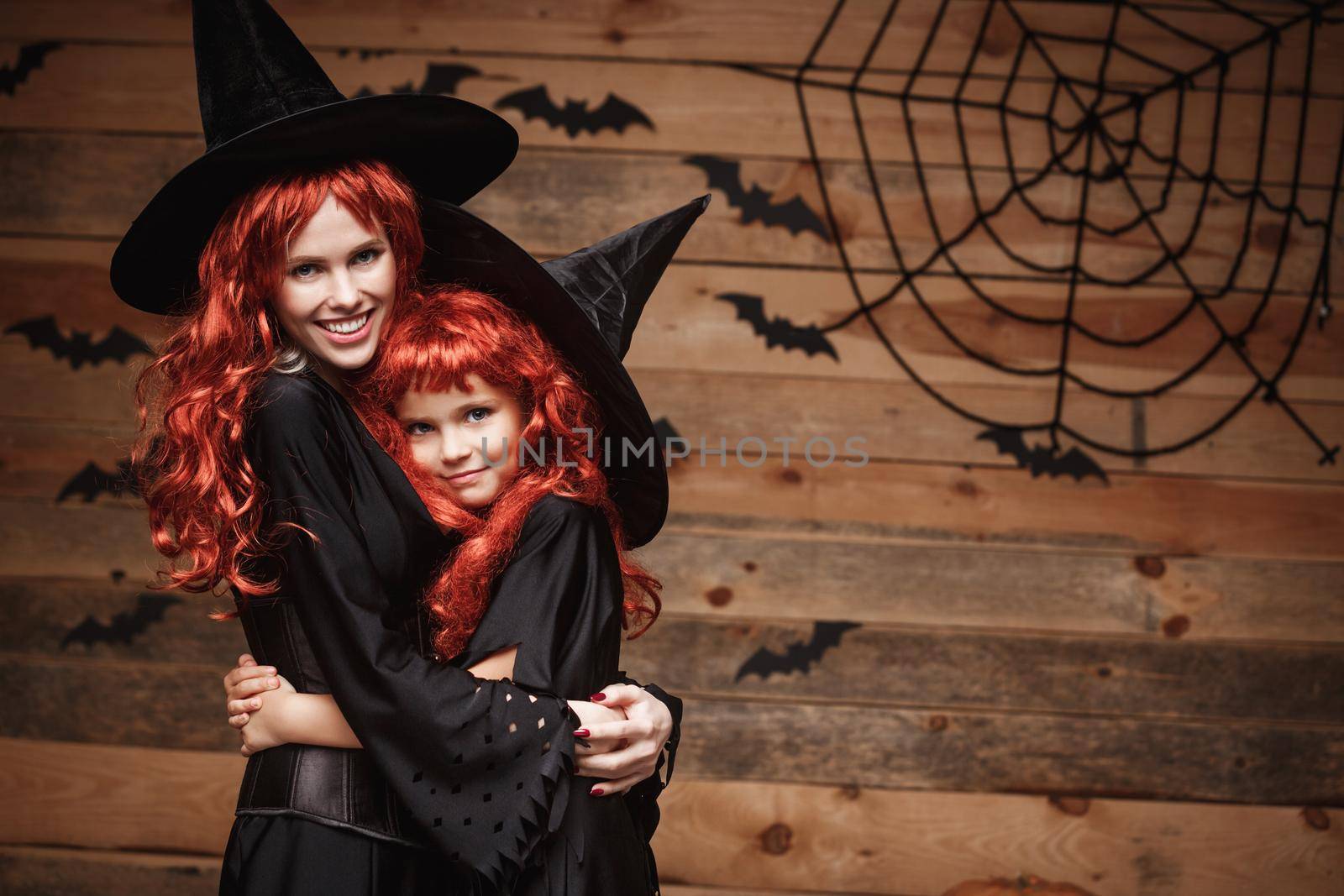 Halloween Concept - Beautiful caucasian mother and her daughter with long red hair in witch costumes happy smiling and hug each other