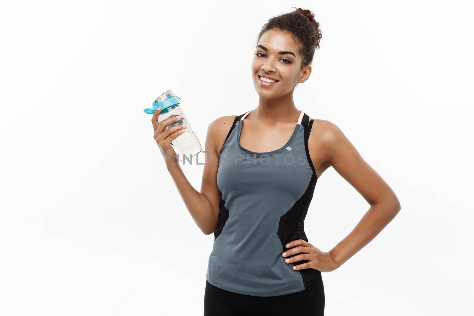 Healthy and Fitness concept - beautiful African American girl in sport clothes holding water bottle after workout. Isolated on white studio background.