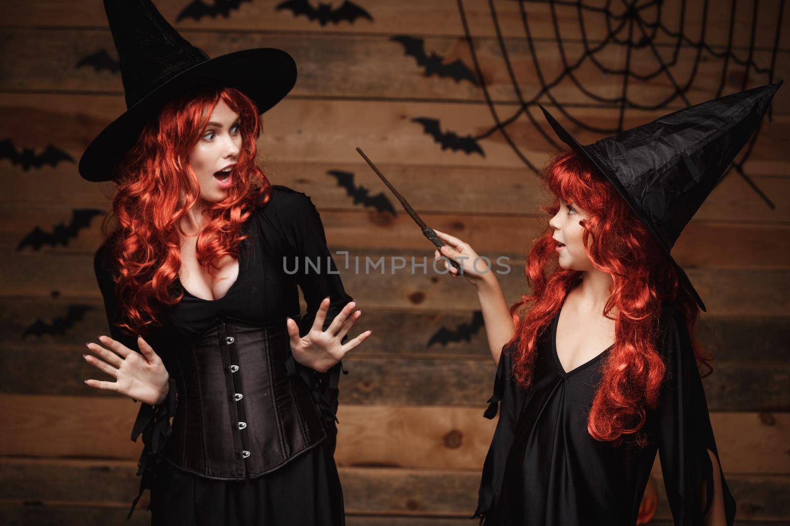 Halloween Concept - little red hair witch using magic with magic wand to her mother with shocked expression. by Benzoix