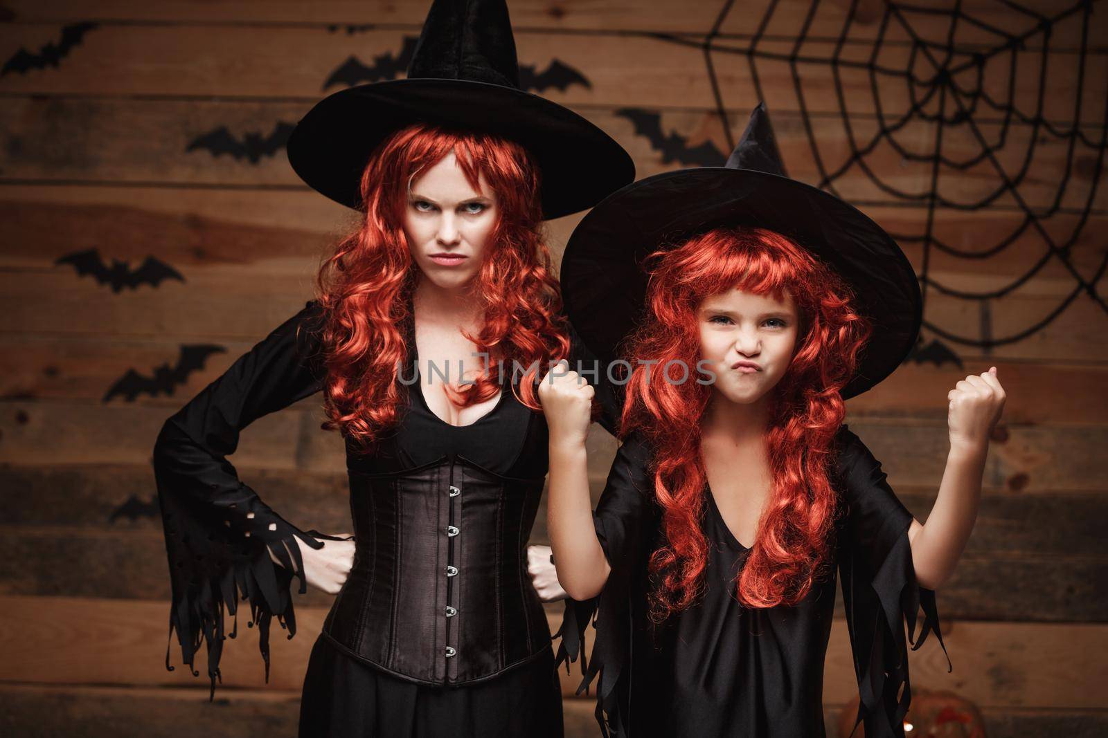 Halloween Concept - Beautiful caucasian mother and her daughter with long red hair in witch costumes witch cheerful fighting facial expression