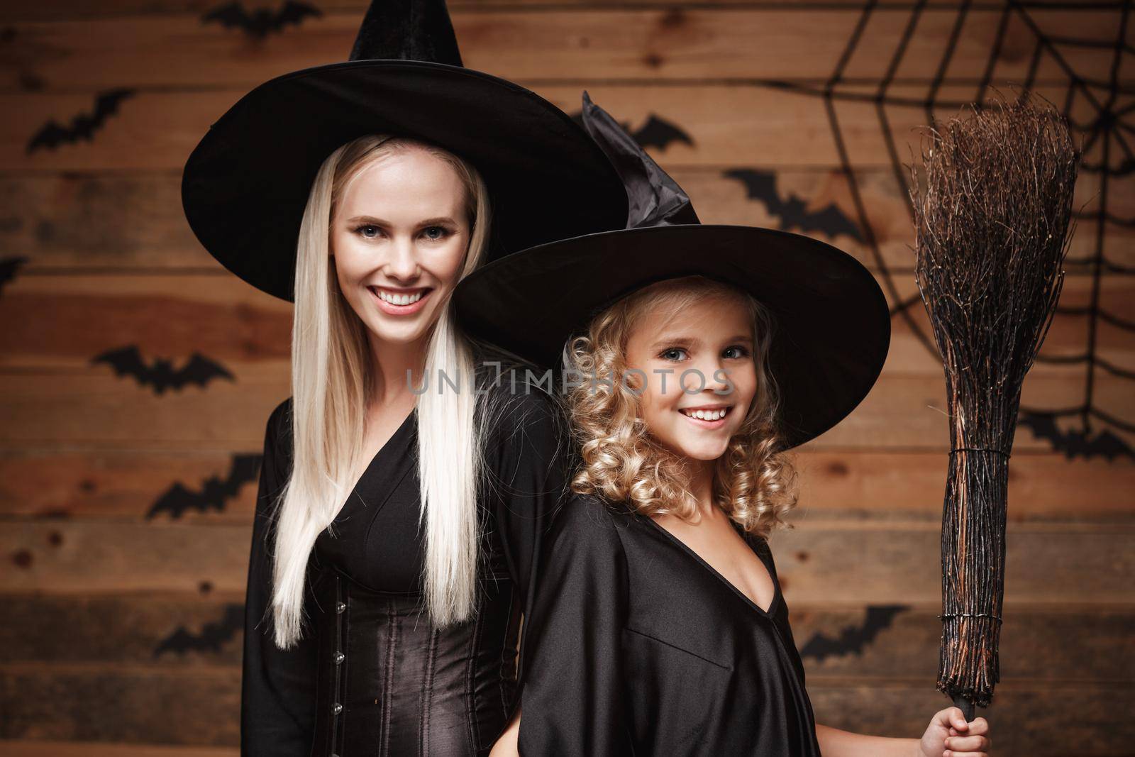 Halloween Concept - Closeup beautiful caucasian mother and her daughter in witch costumes celebrating Halloween posing with curved pumpkins over bats