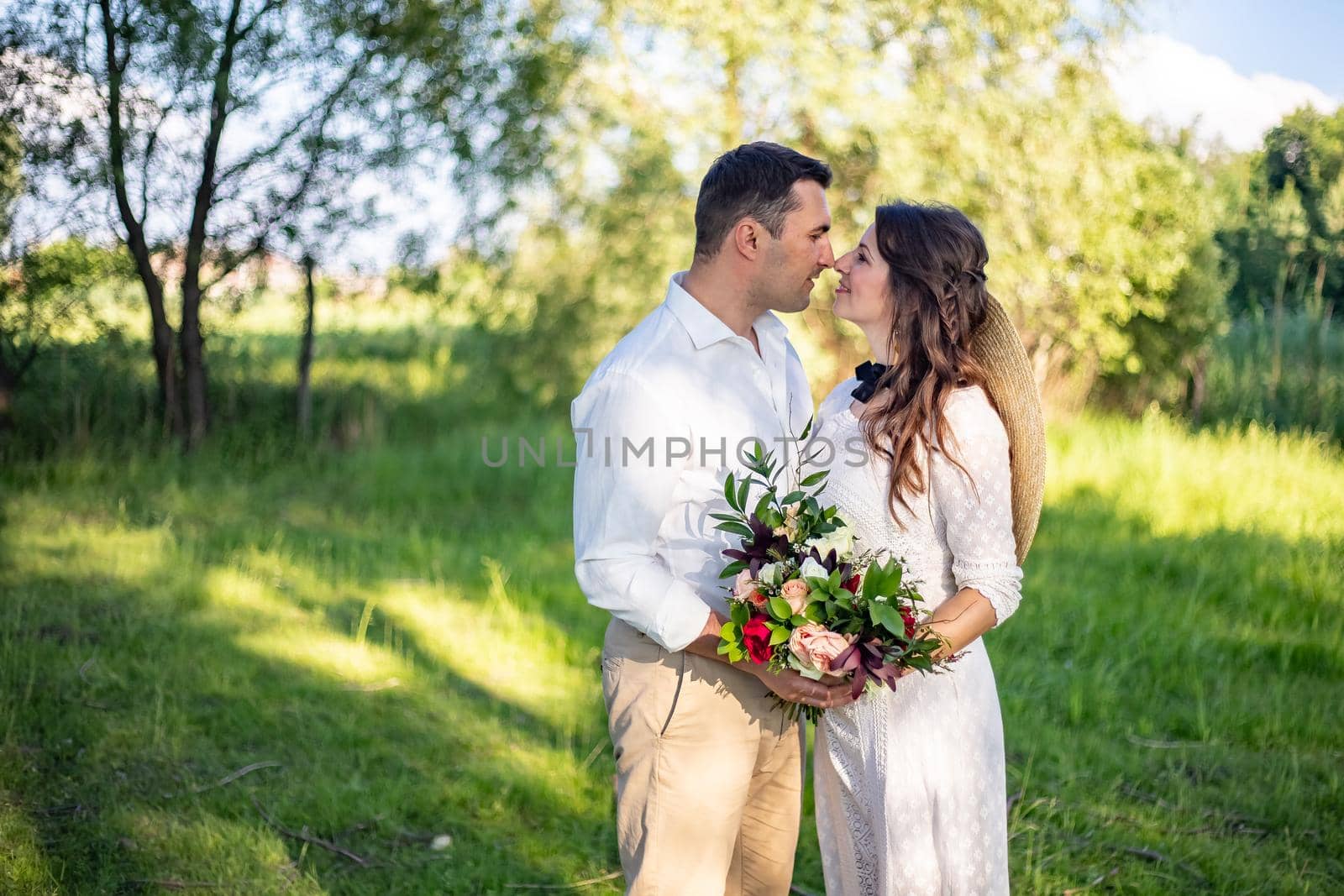 beautiful newlyweds stand on a green meadow and kiss, rustic style wedding by Anyatachka