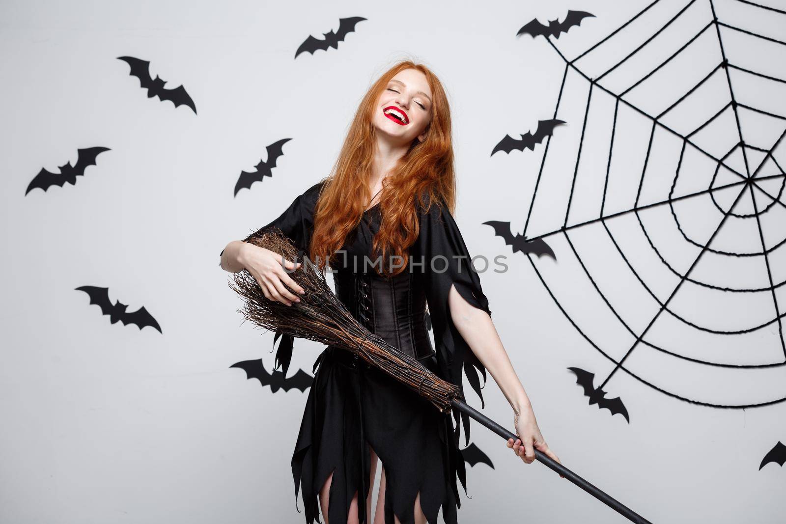 Halloween Concept - Happy elegant witch enjoy playing with broomstick halloween party over grey background. by Benzoix