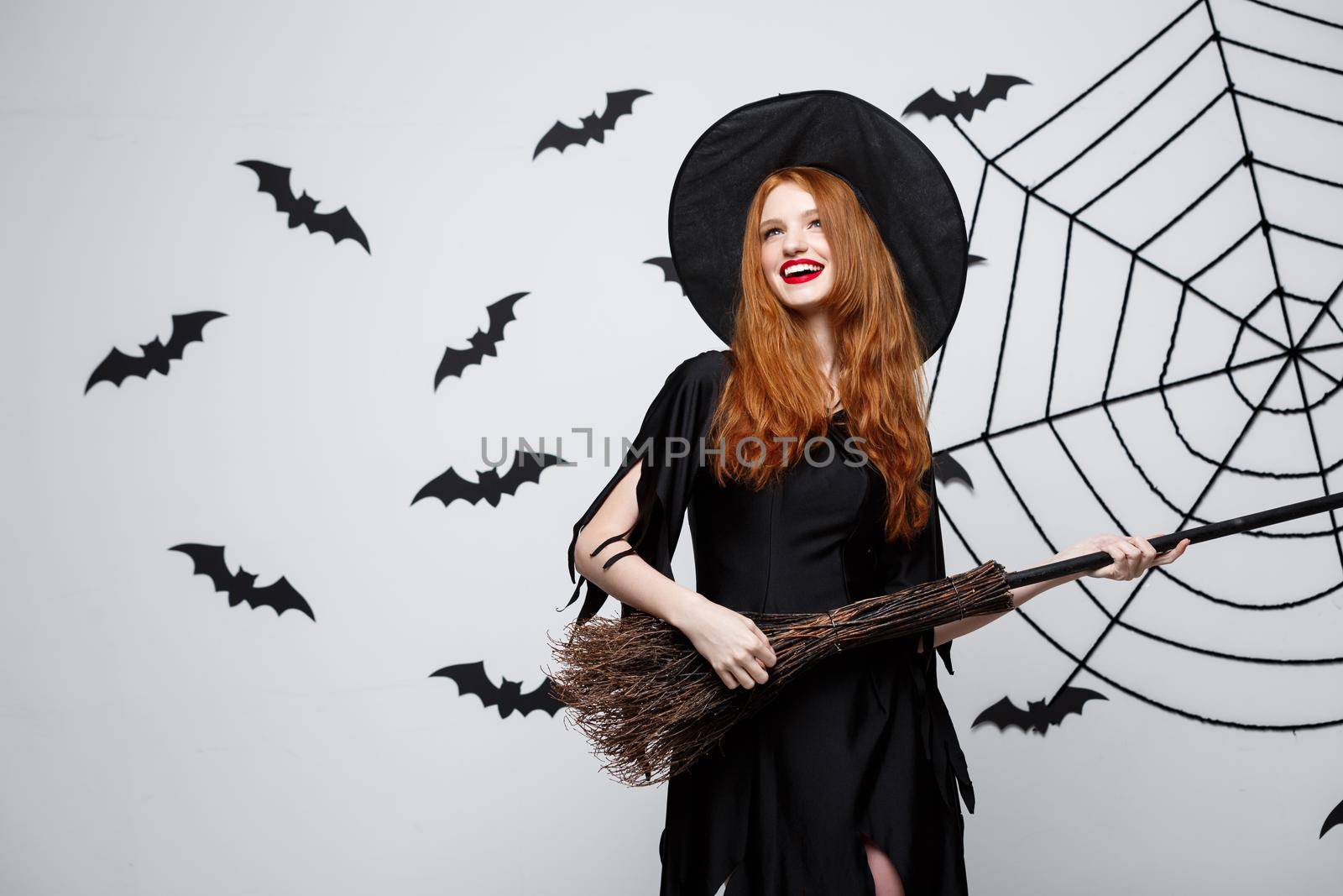 Halloween Concept - Happy elegant witch enjoy playing with broomstick halloween party over grey background