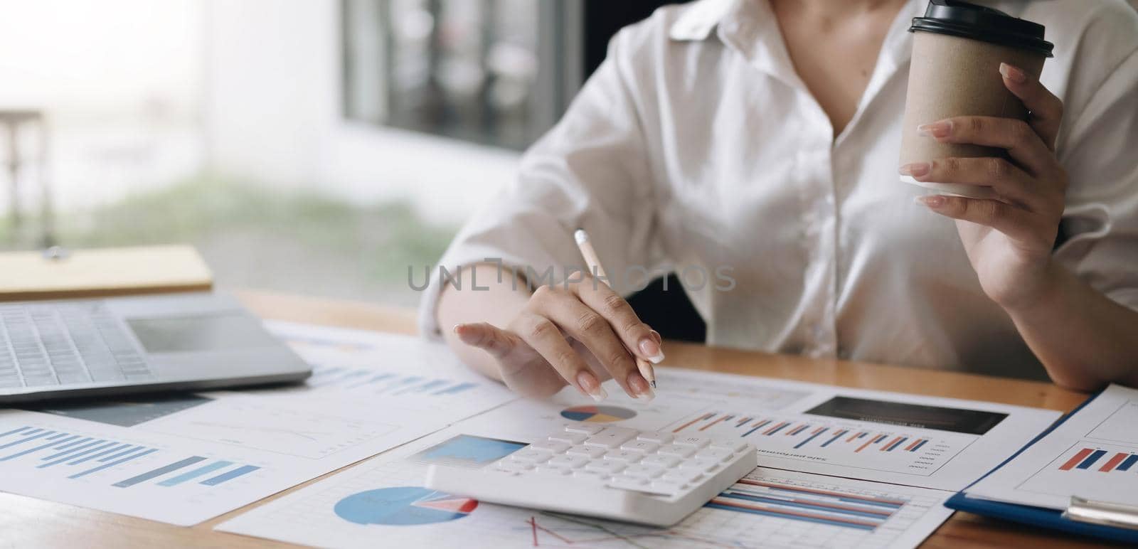 Close up Business woman using calculator and laptop for do math finance on wooden desk in office and business working background, tax, accounting, statistics and analytic research concept.