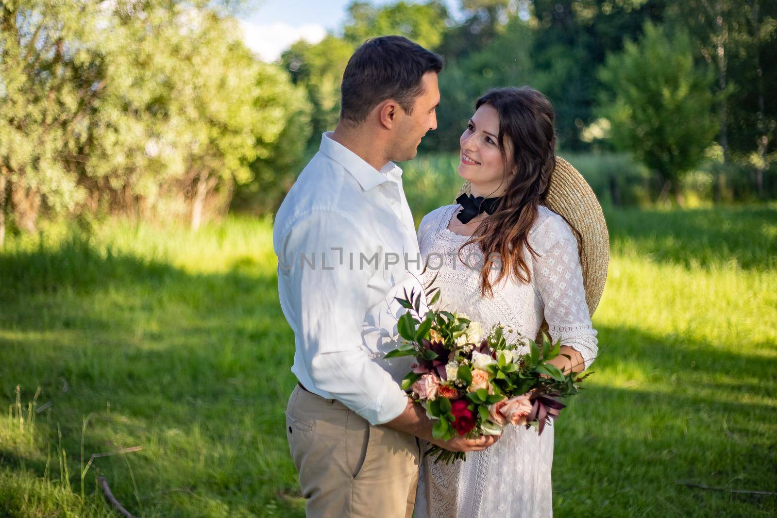 Happy young people in wedding attire stand in the meadow and look at each other by Anyatachka
