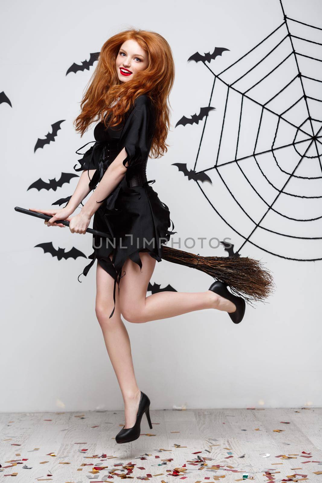 Halloween Concept - Happy elegant witch enjoy playing with broomstick halloween party over grey background